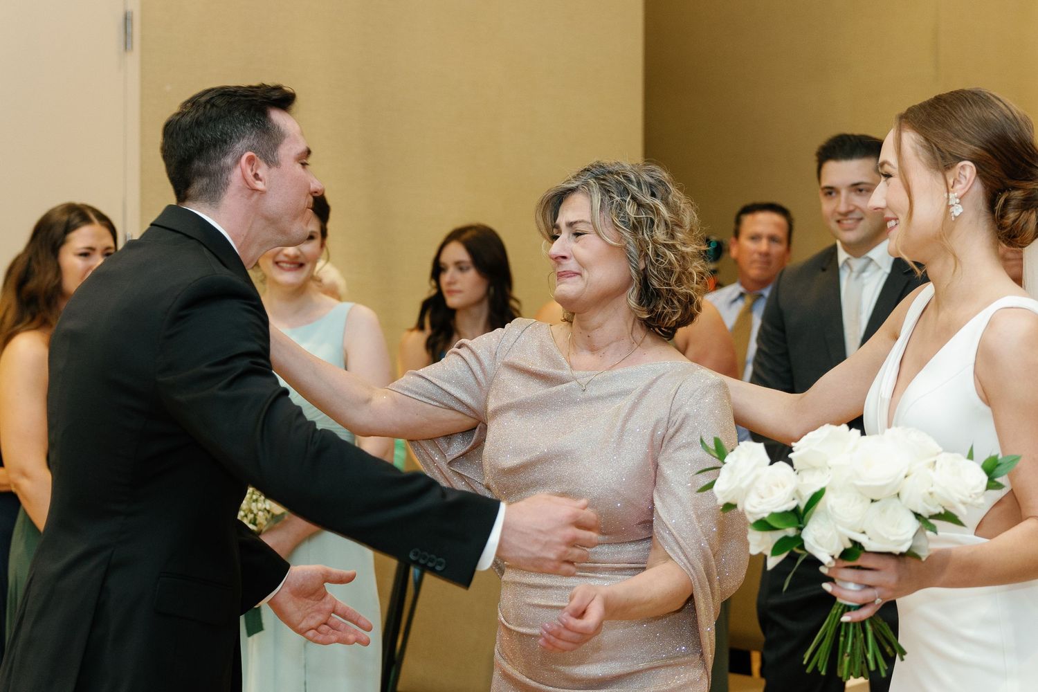 Wedding guests dance and embrace on a crowded dance floor during a reception celebration.