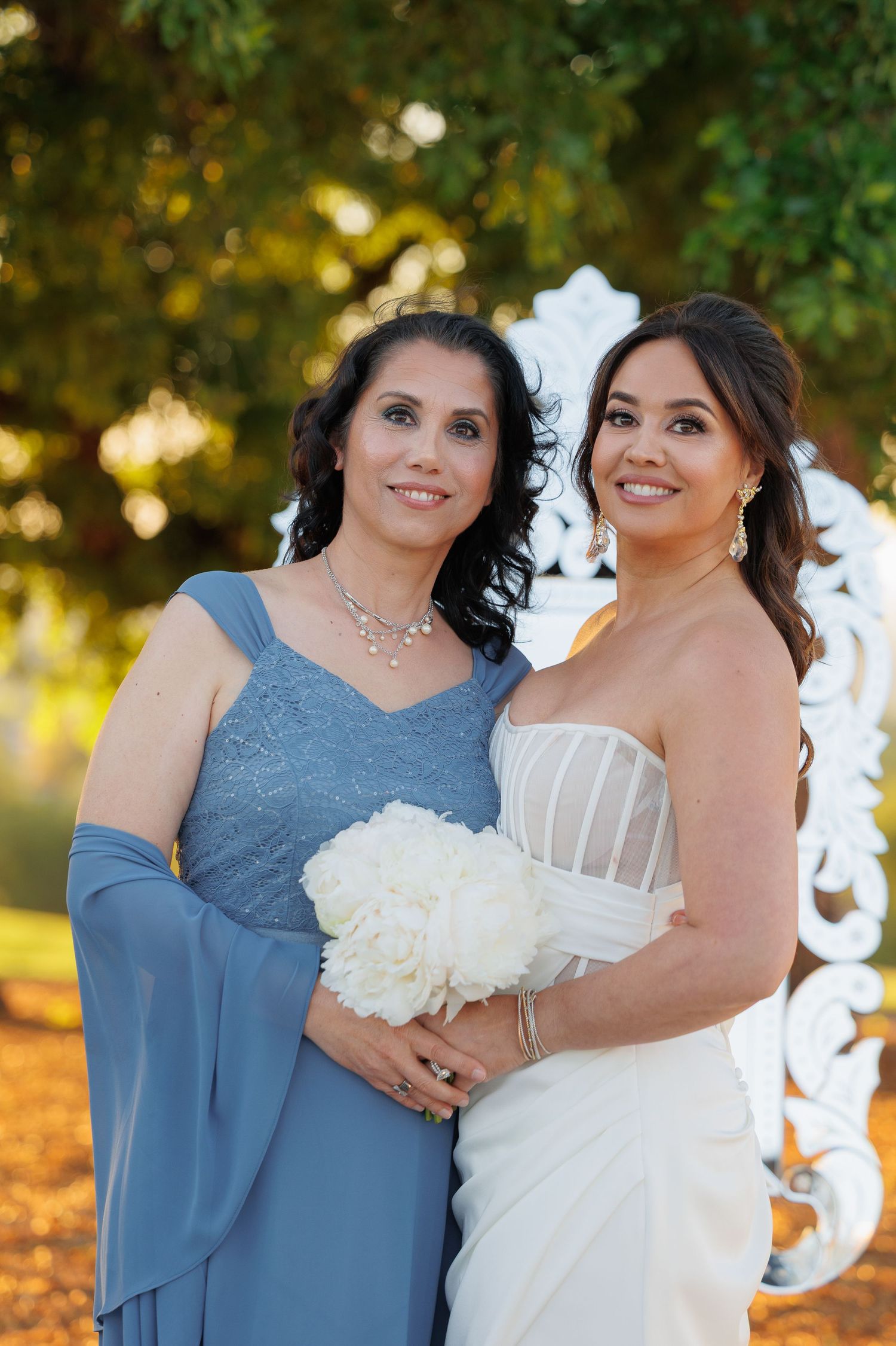 A bride in a white gown and companion in blue dress pose together in a series of outdoor wedding photos at sunset.