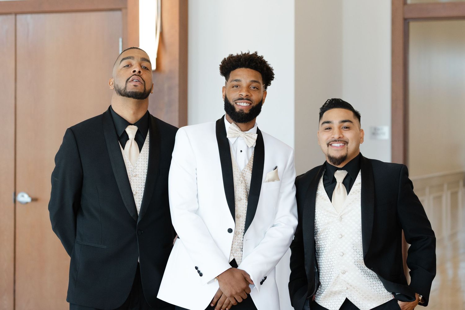 A group of formally dressed men in black suits and white tuxedos pose together for a wedding photo.