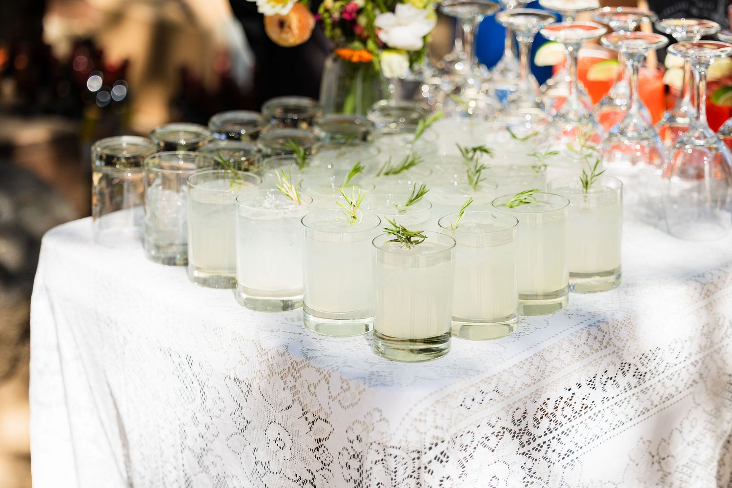Fresh lemonade cocktails garnished with herbs arranged on a white lace tablecloth at an elegant event.