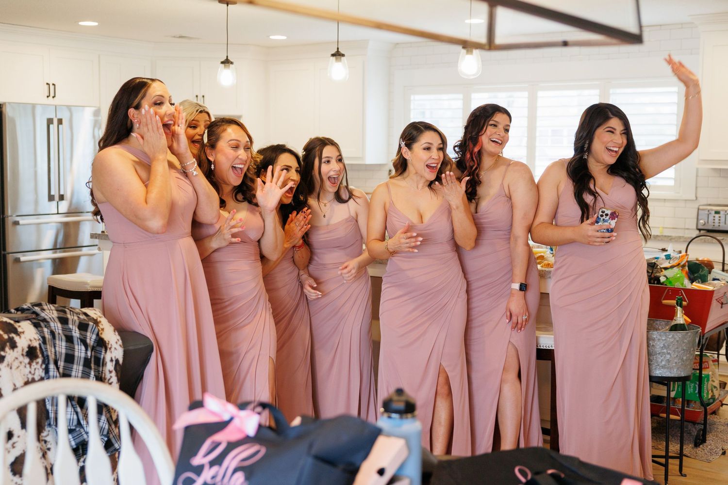 Wedding party in matching dusty rose dresses celebrates joyfully in an elegant indoor venue.