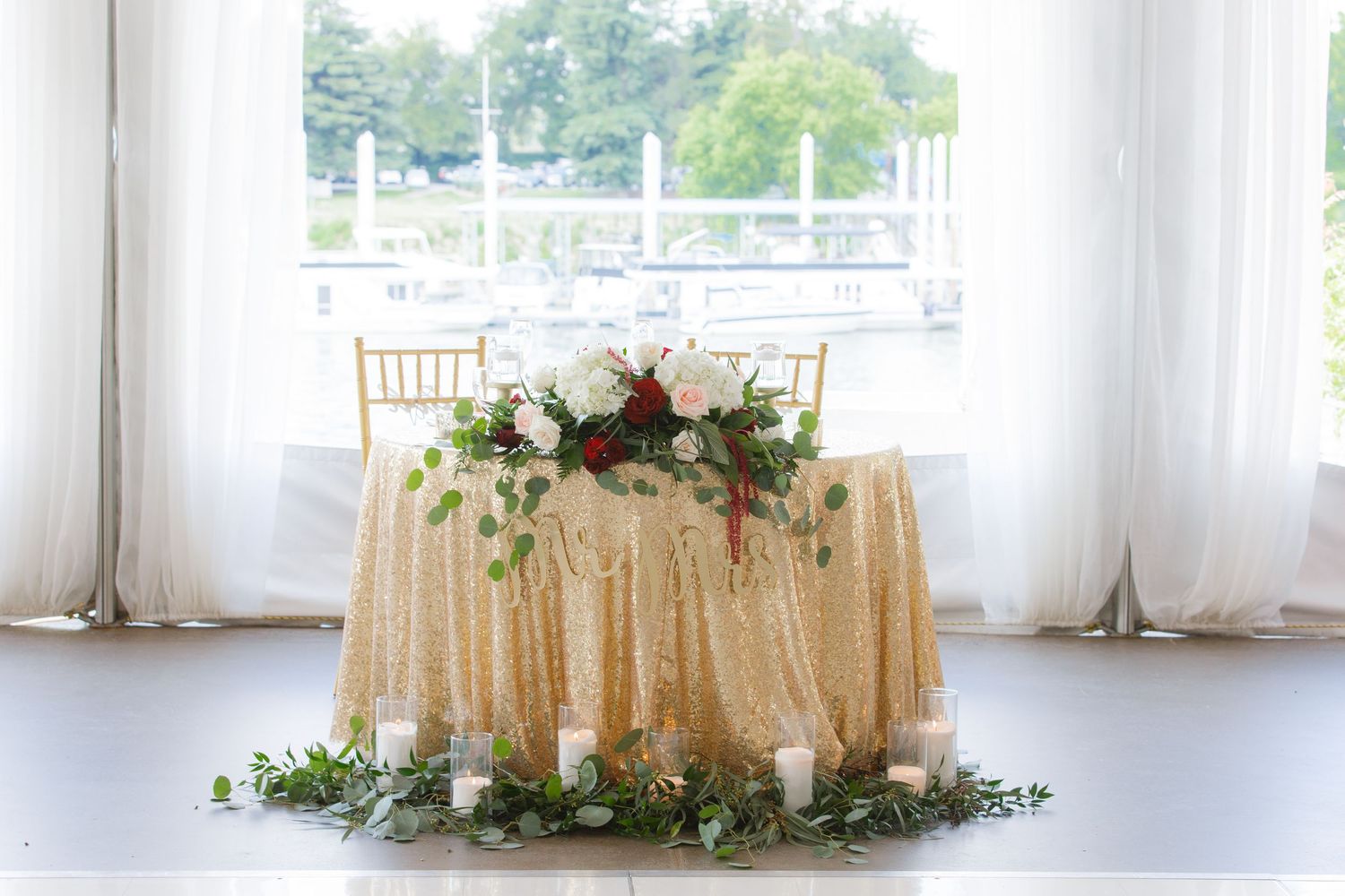 Elegant wedding reception table setup with champagne colored tablecloths and floral arrangements near bright windows.