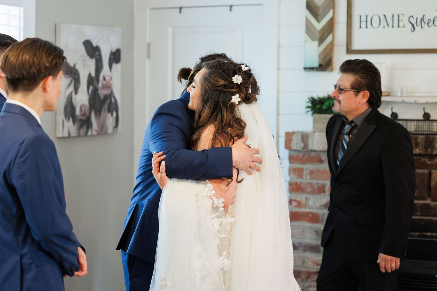 A wedding scene in a rustic home interior with a long white veil and navy blue attire.