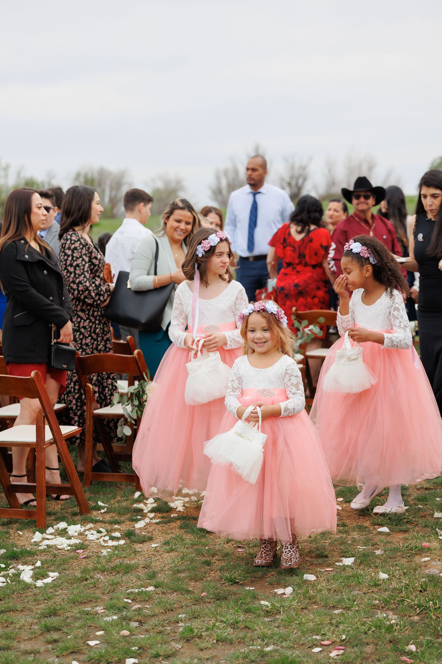 Flower girls in pink tulle skirts scatter petals during an outdoor wedding ceremony.