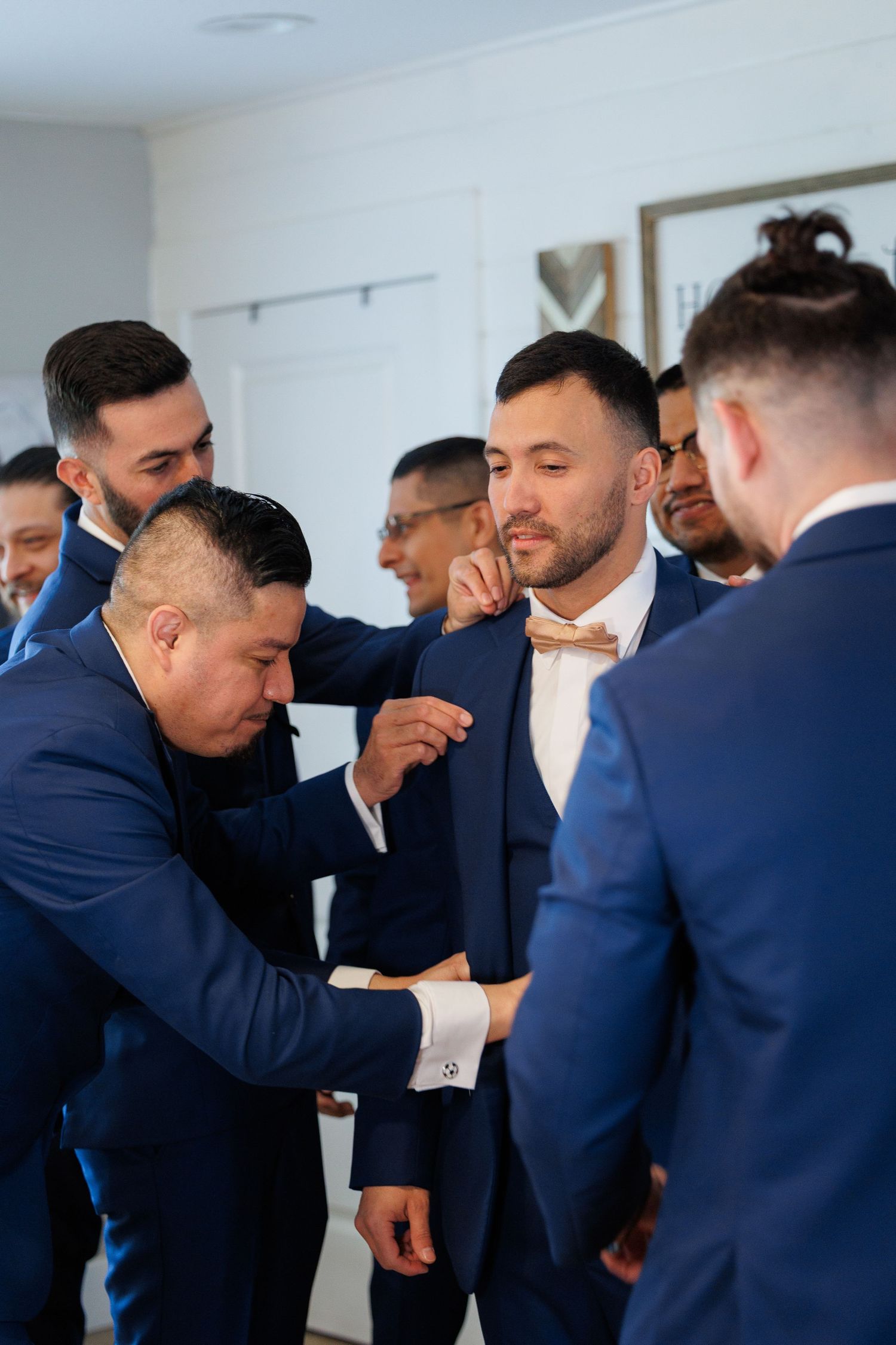 A sequence of emotional moments showing men in navy suits embracing during what appears to be a wedding celebration.
