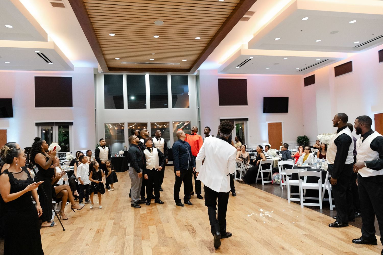 A panoramic view of a modern dance studio with wooden floors and mirrored walls filled with people during an event.