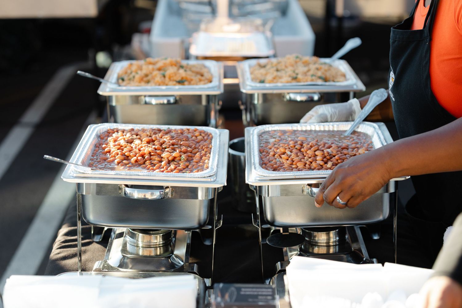 Stainless steel chafing dishes filled with food being served at a buffet line.