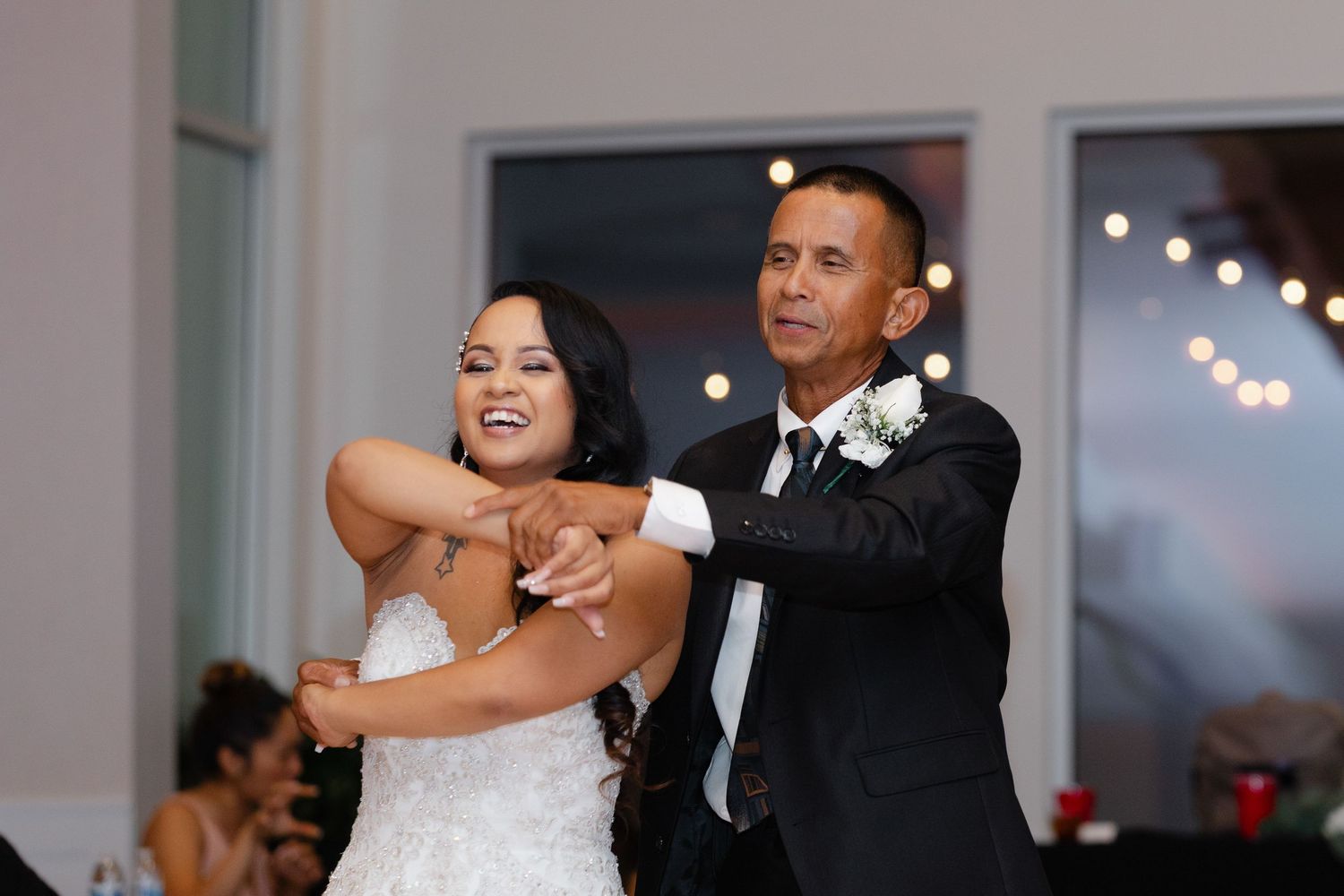 A couple shares their first dance together at a wedding reception with twinkling lights in the background.