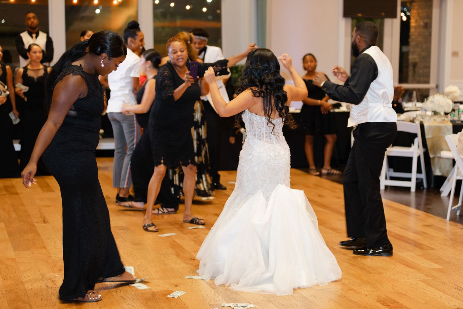 Dancers in formal attire move across a wooden dance floor at an elegant event with string lights overhead.