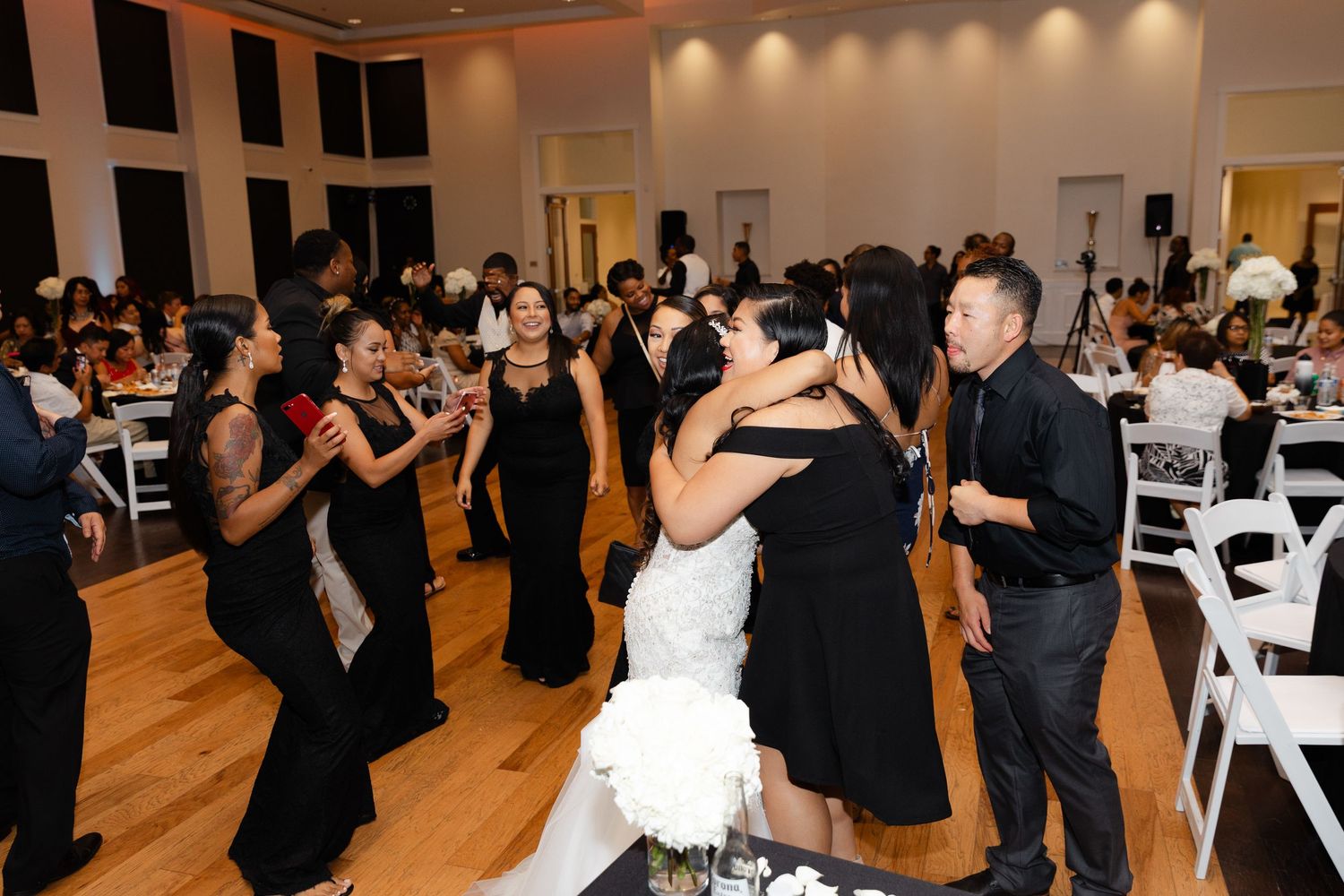 Guests in formal black attire dancing and mingling at an elegant indoor event with warm lighting and wooden floors.