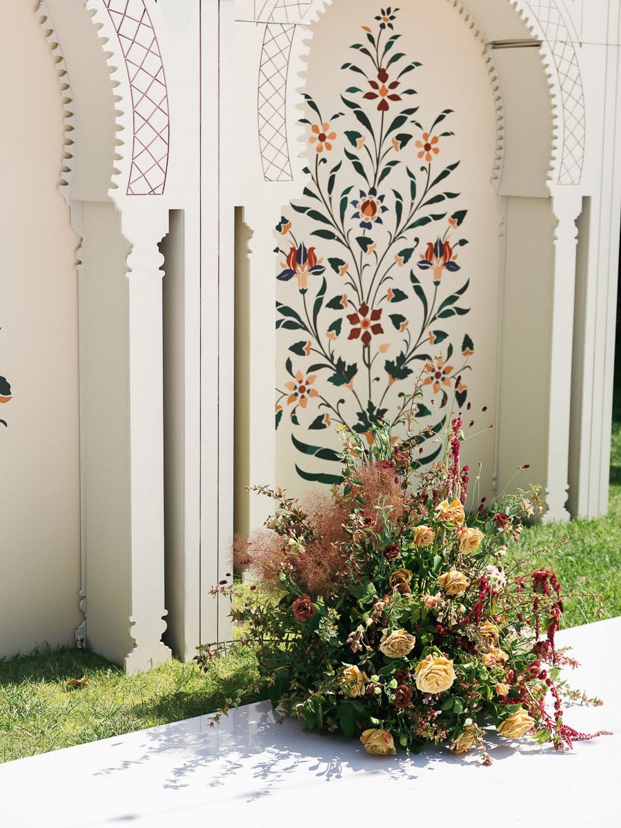 Elegant floral wall art with inlaid design and ornate arches framed by white columns, accented by a lush garden arrangement.