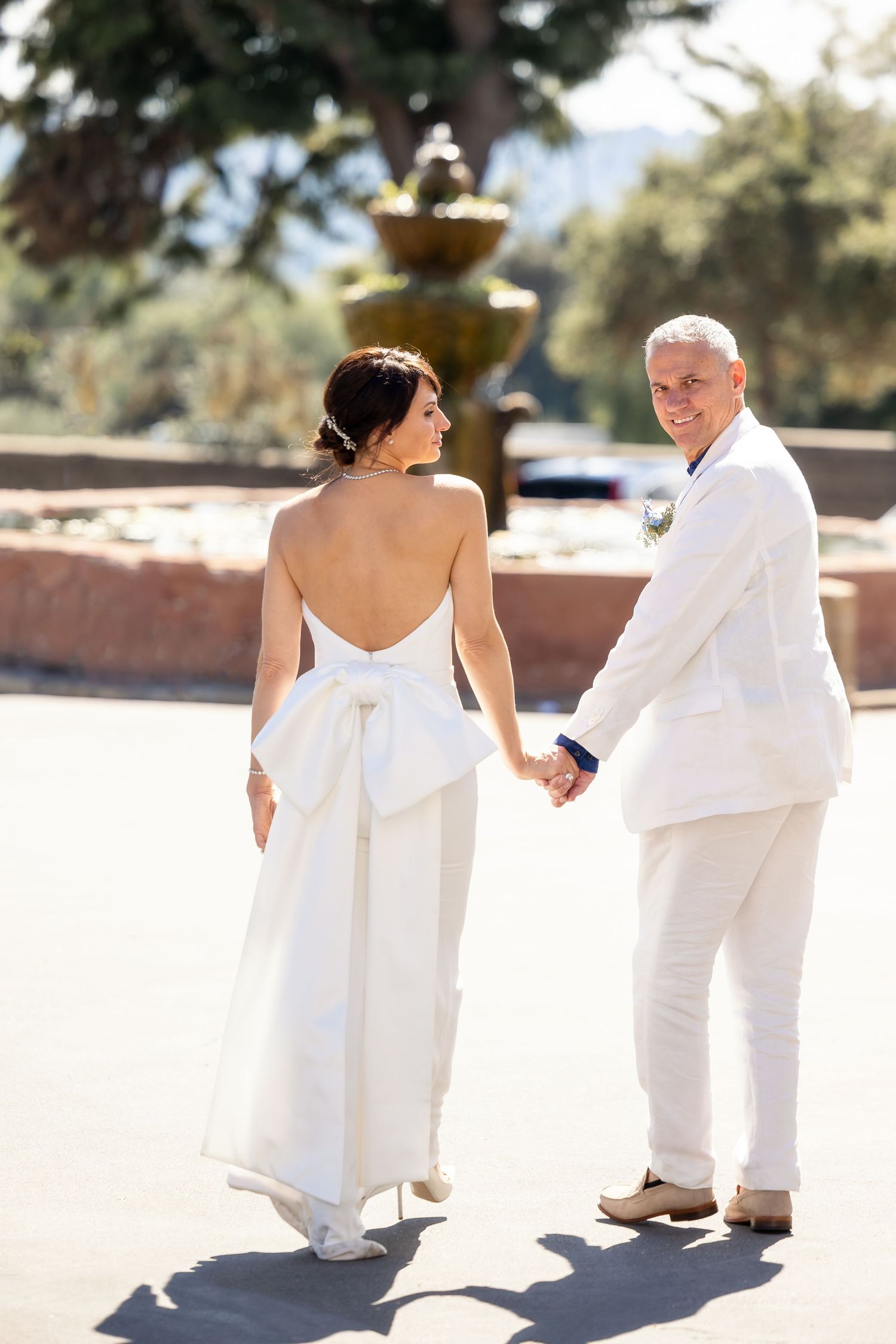 Couple in all-white attire walking together during outdoor wedding photo session.