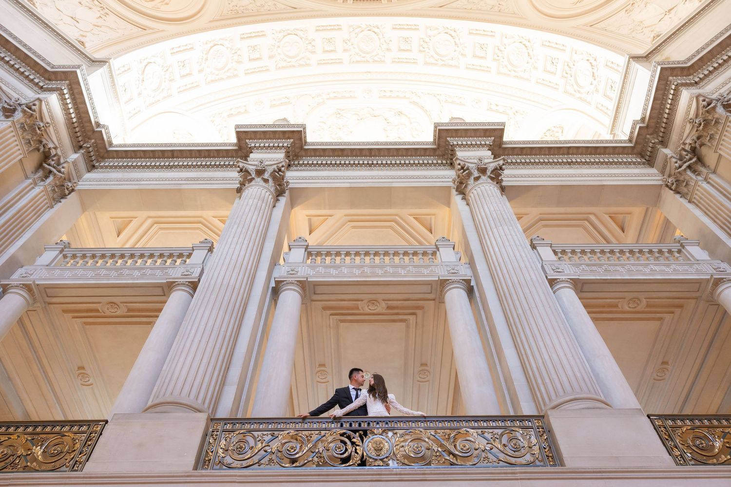 Couple embracing on ornate balcony with grand columns at San Francisco City Hall wedding.