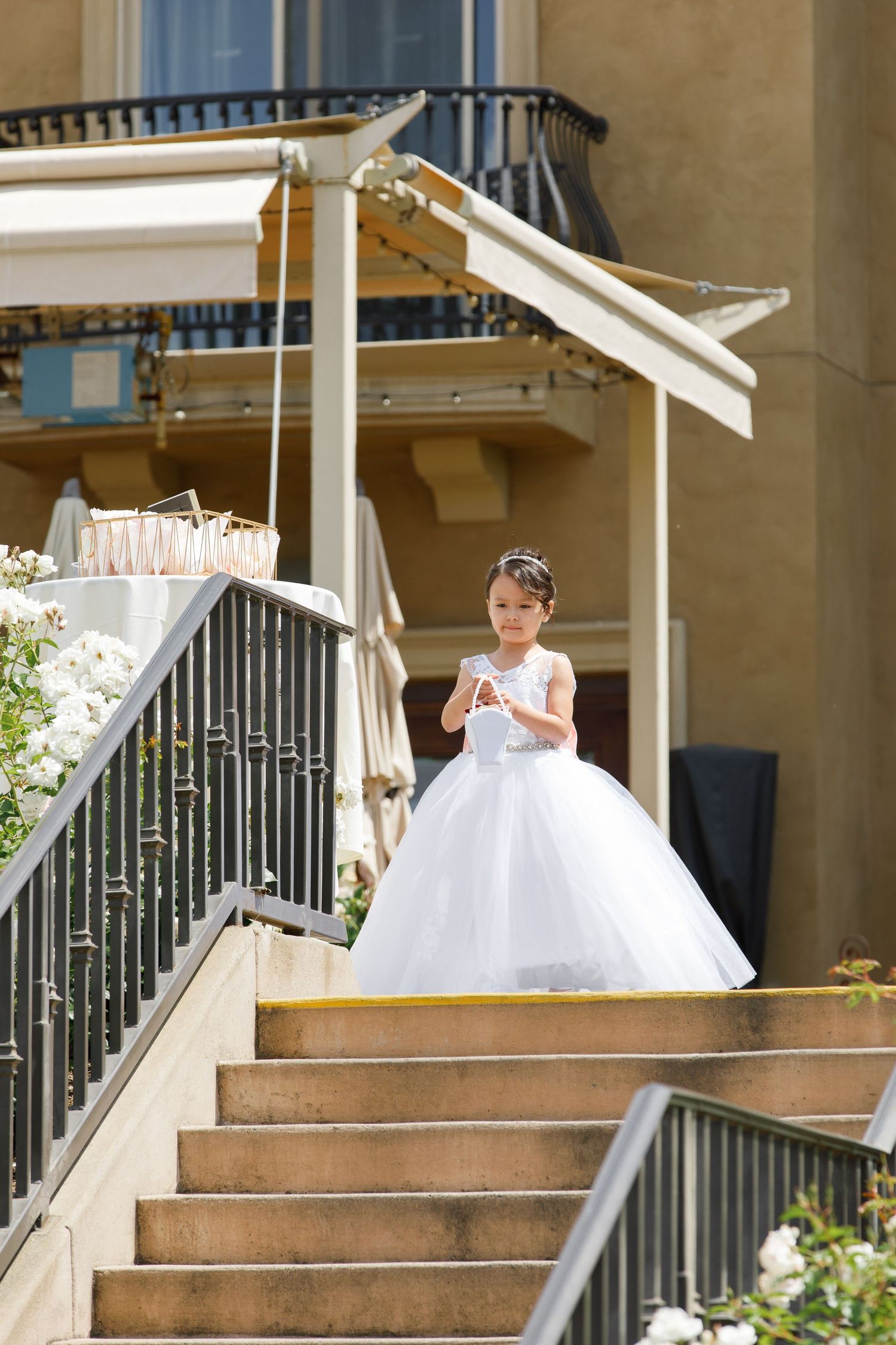 A young person in an elegant white ball gown stands at the top of outdoor stone stairs at an elegant venue.