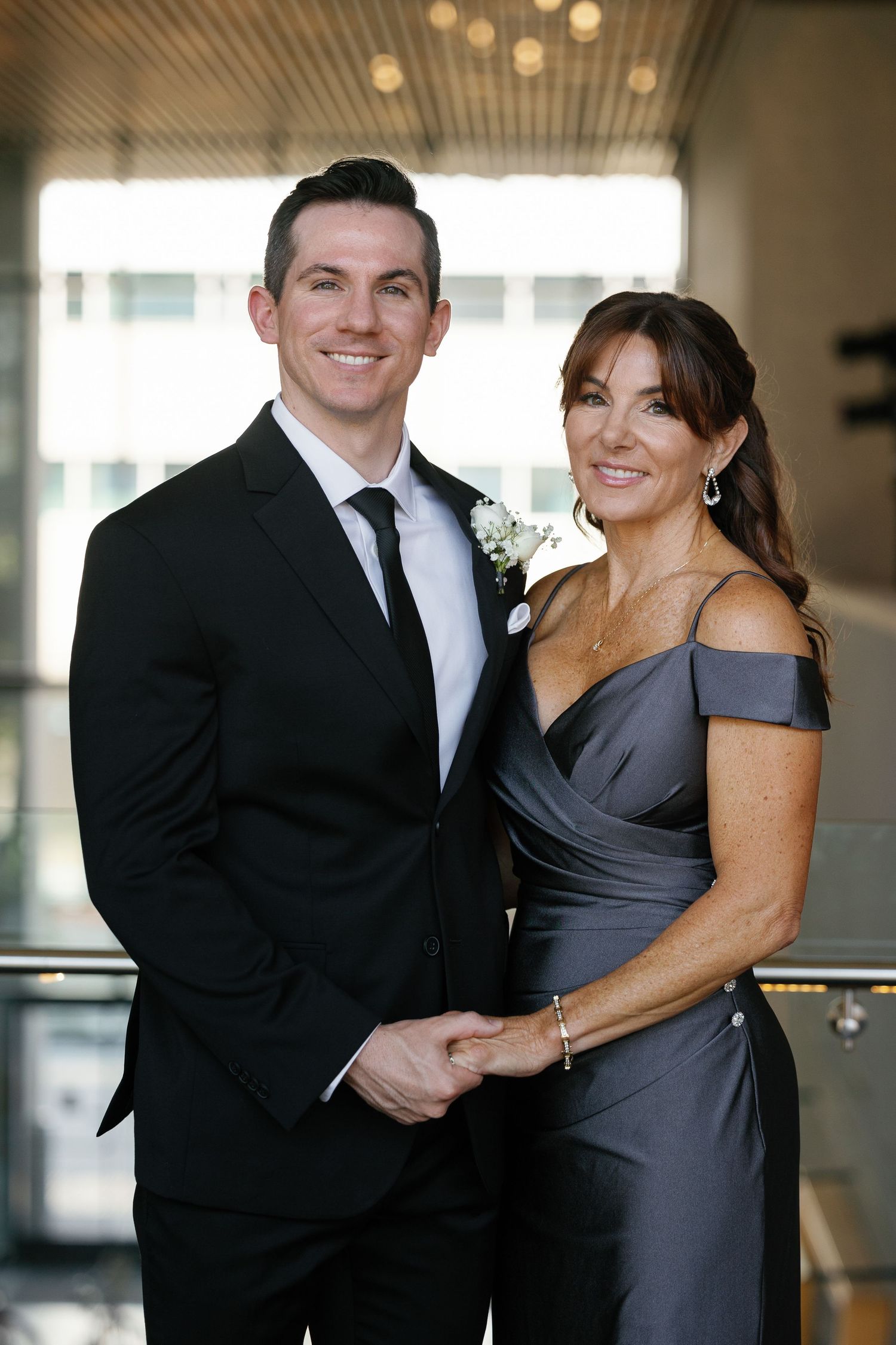 A couple in formal attire, with the man in a black suit and woman in a gray dress, pose together for photos.