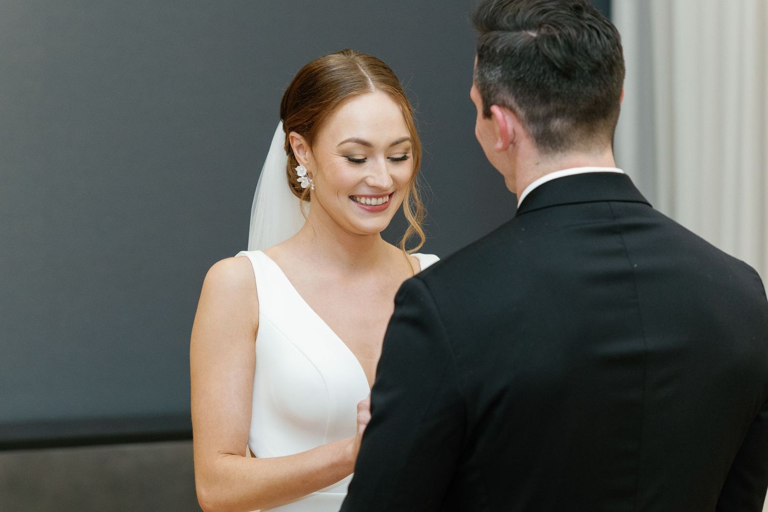 A bride and groom share an intimate moment during their wedding ceremony in front of white curtains.