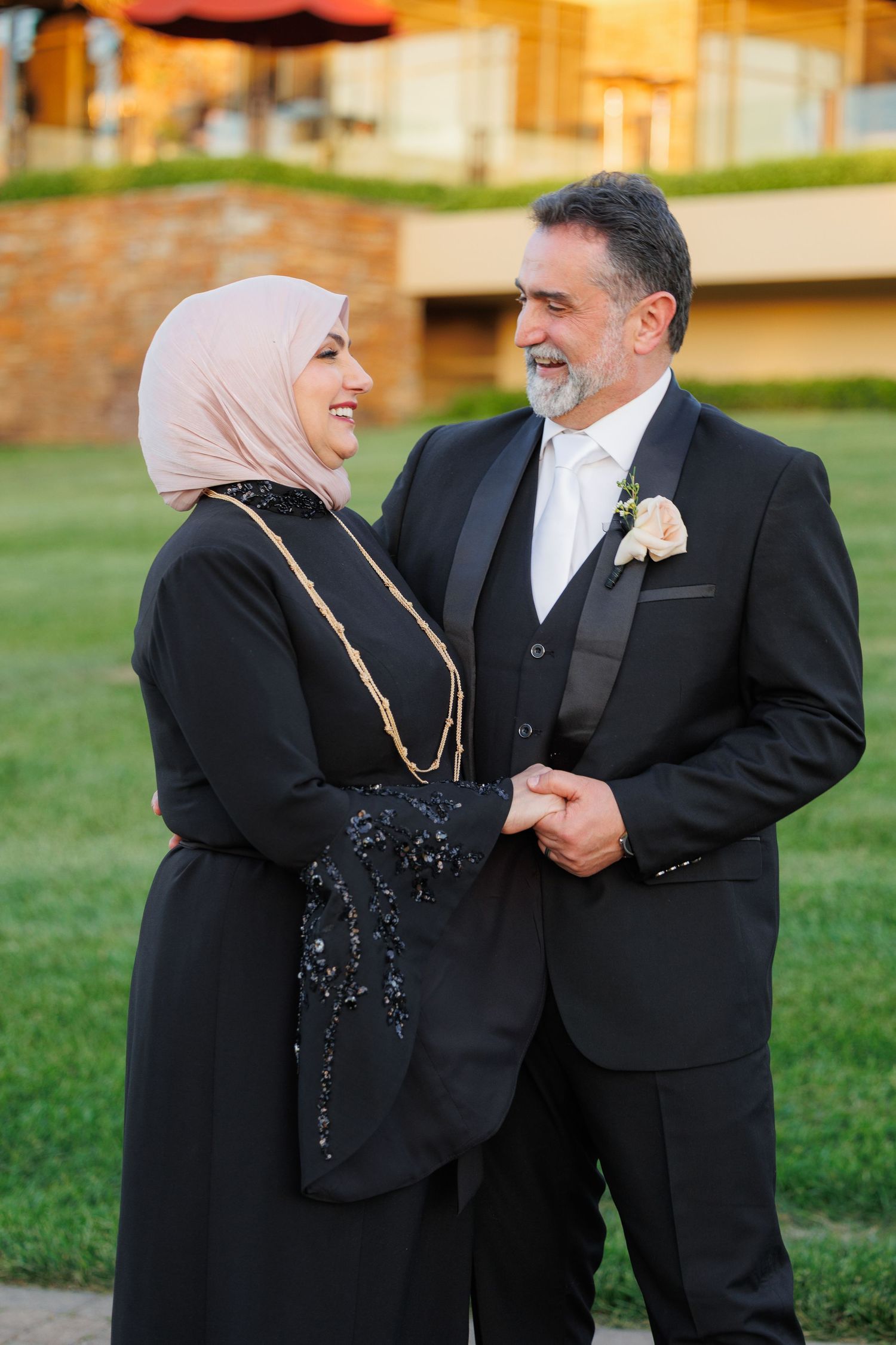 A couple in formal attire share a tender moment together on a grassy lawn.