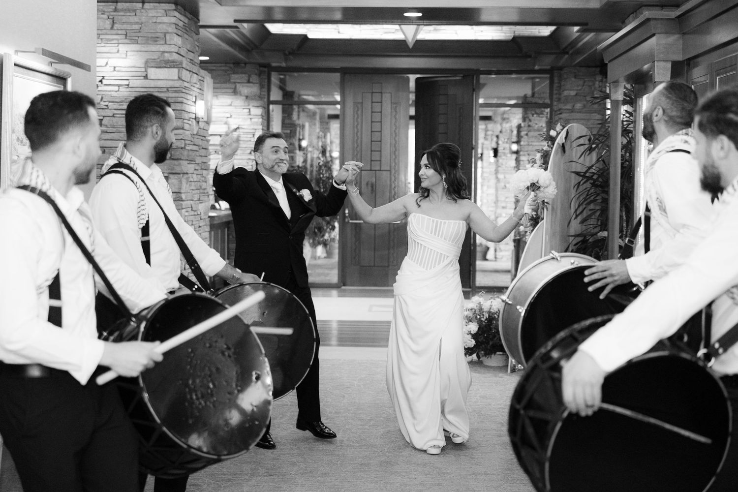A black and white panoramic photo showing a wedding celebration with guests dancing and mingling at a reception.