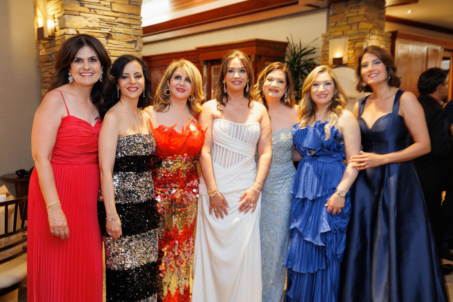 A group of women in formal evening attire pose together at a social event.