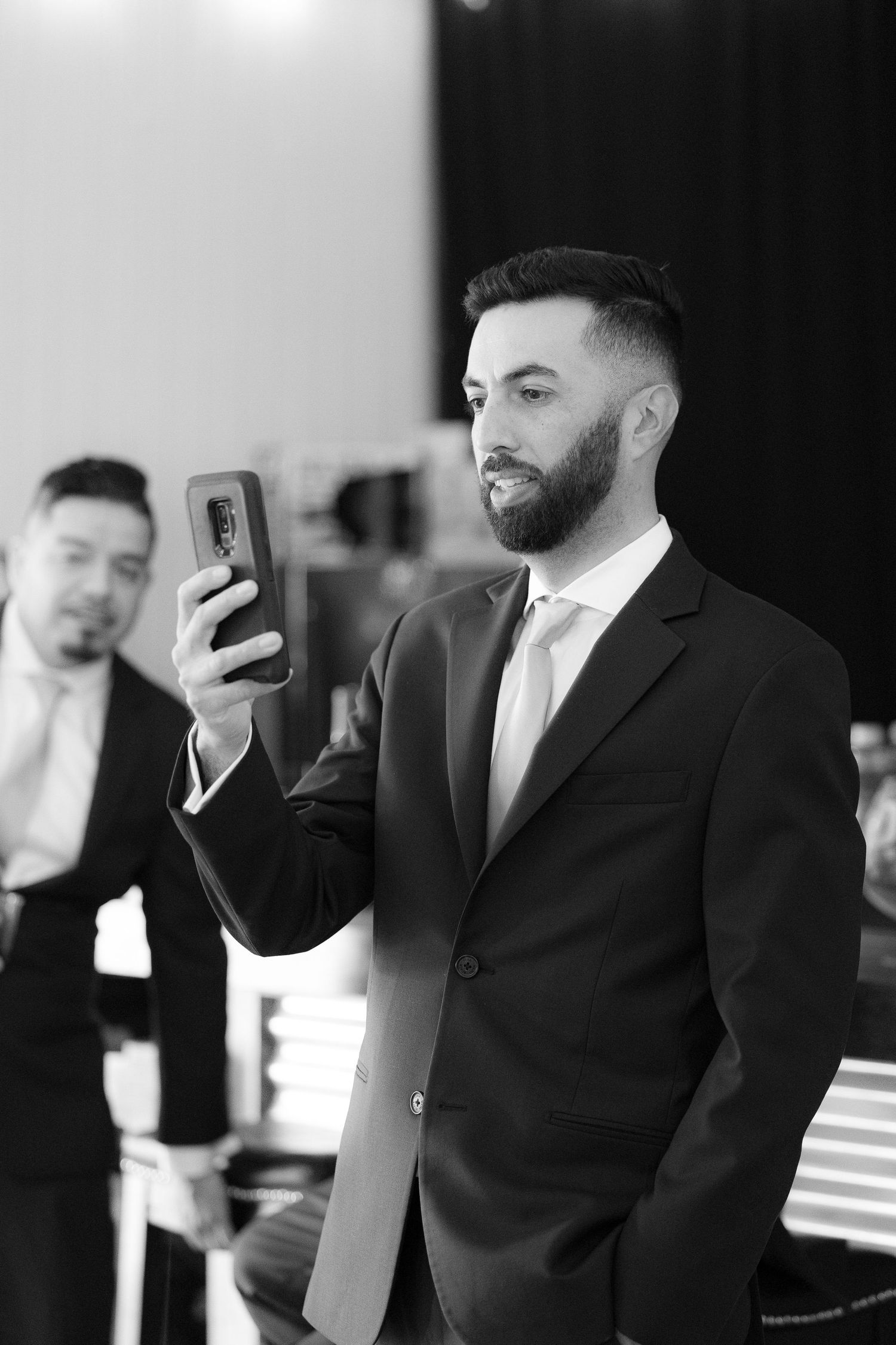 A well-dressed man in a black suit and tie looks at his mobile phone during a formal event.