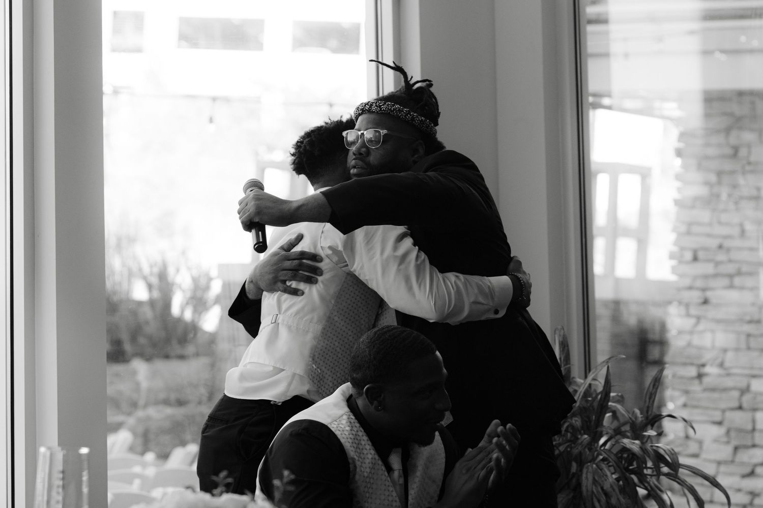 Black and white photograph showing two people embracing in front of a window in a tender emotional moment.