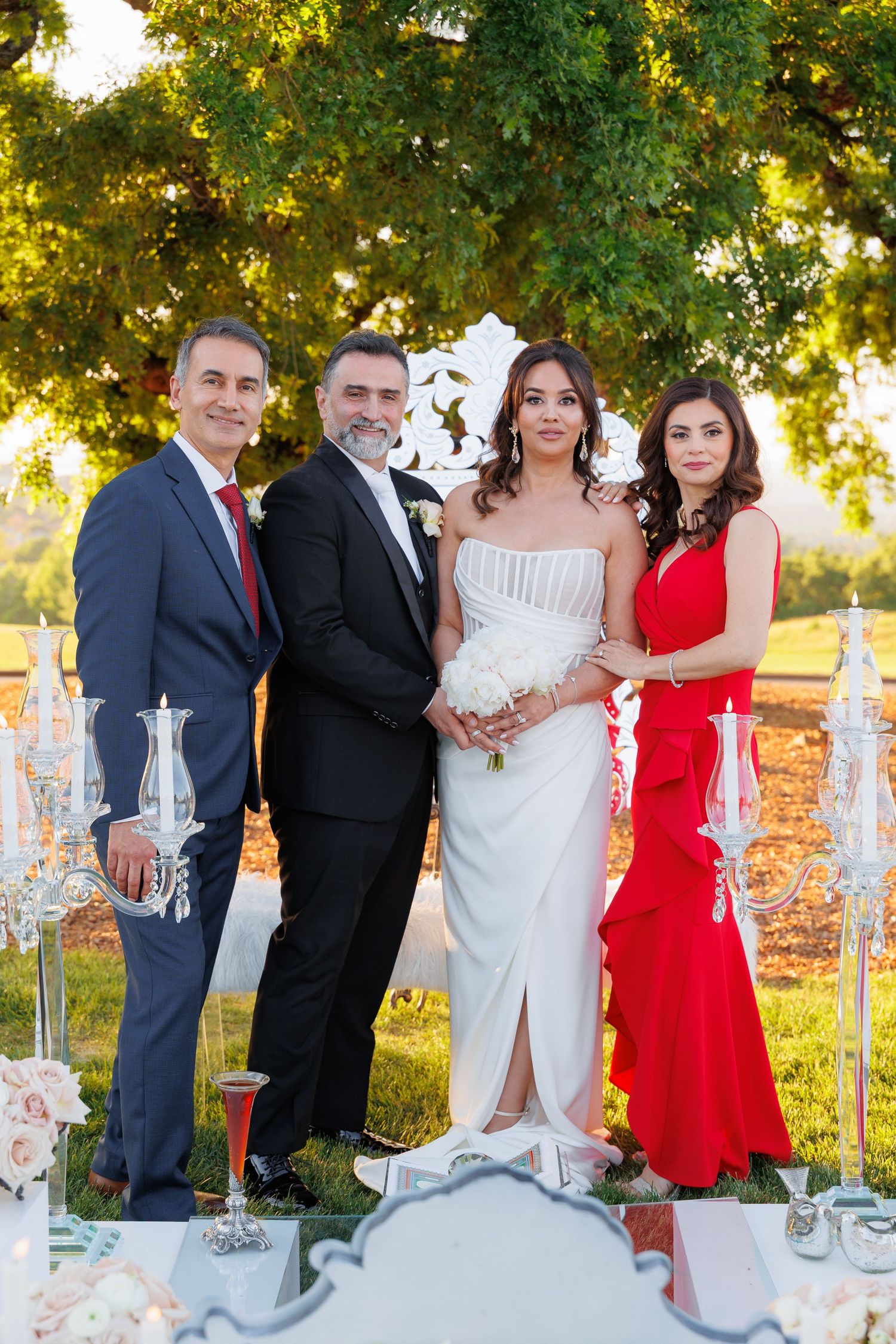 Wedding party stands outdoors at sunset with elegant decor including glass vases and floral arrangements.