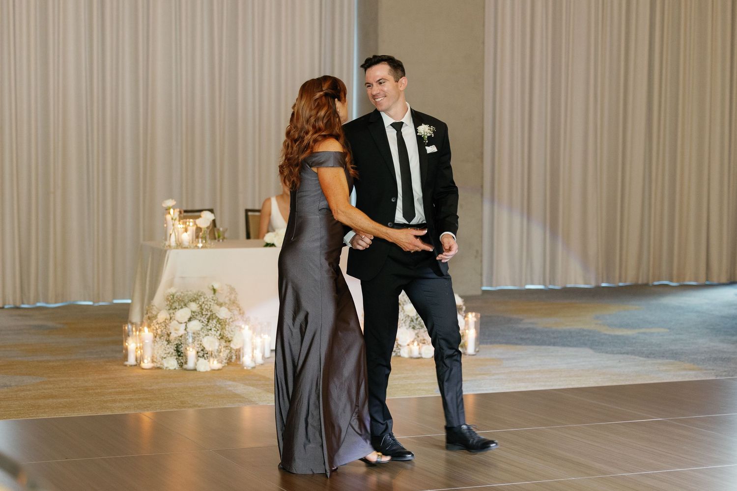 A couple shares a dance together on an elegant ballroom floor with floral decorations in the background.