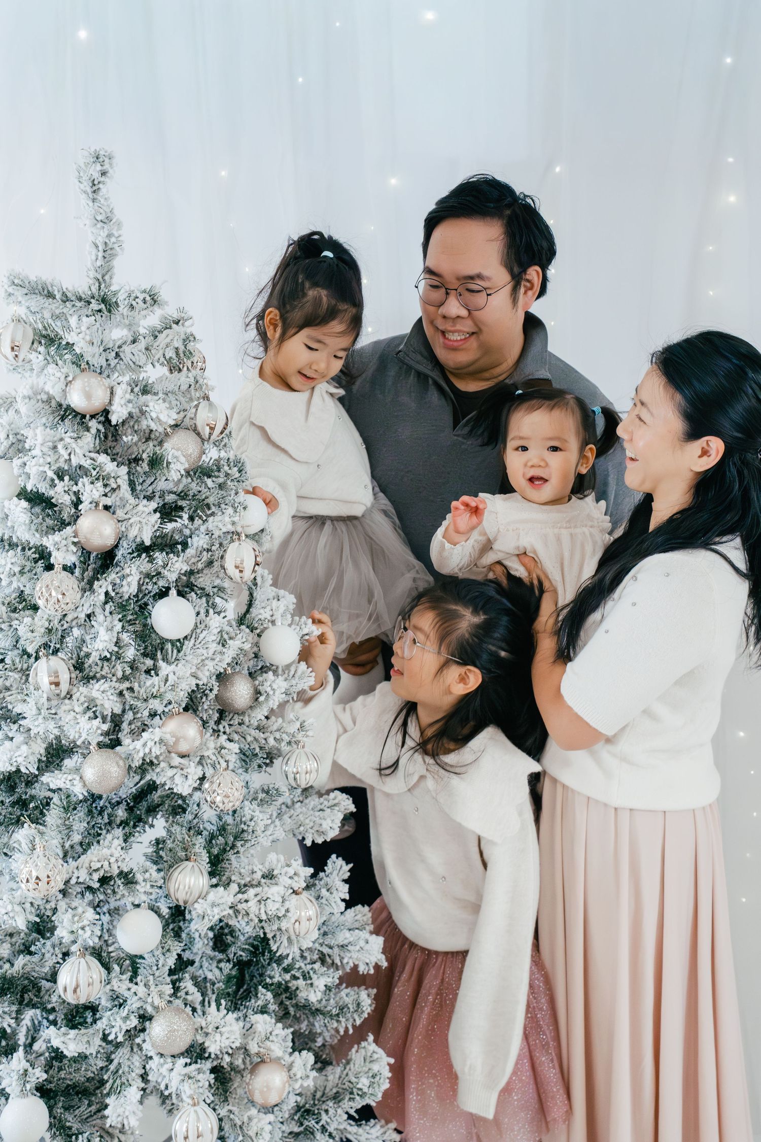 Family of five posing together for a Christmas mini photoshoot in a festive indoor studio with snowy Christmas trees in Kingston, Ontario.
