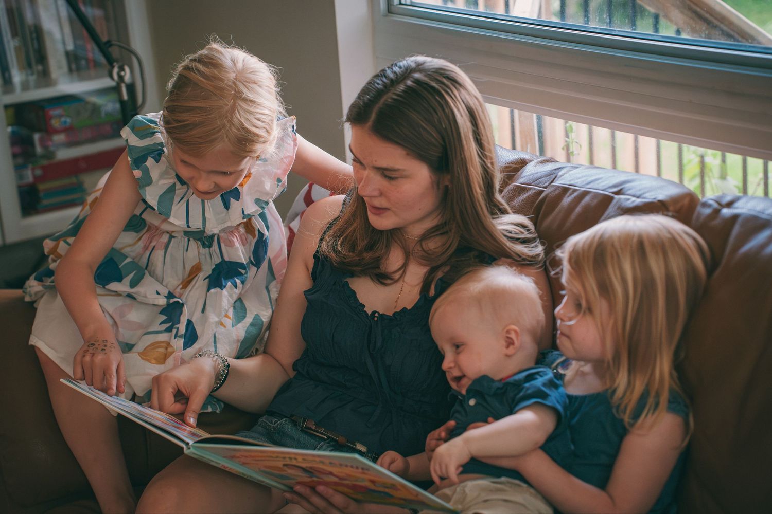 Mother reading a picture book with her three children on the couch during a natural, candid family lifestyle photography session.