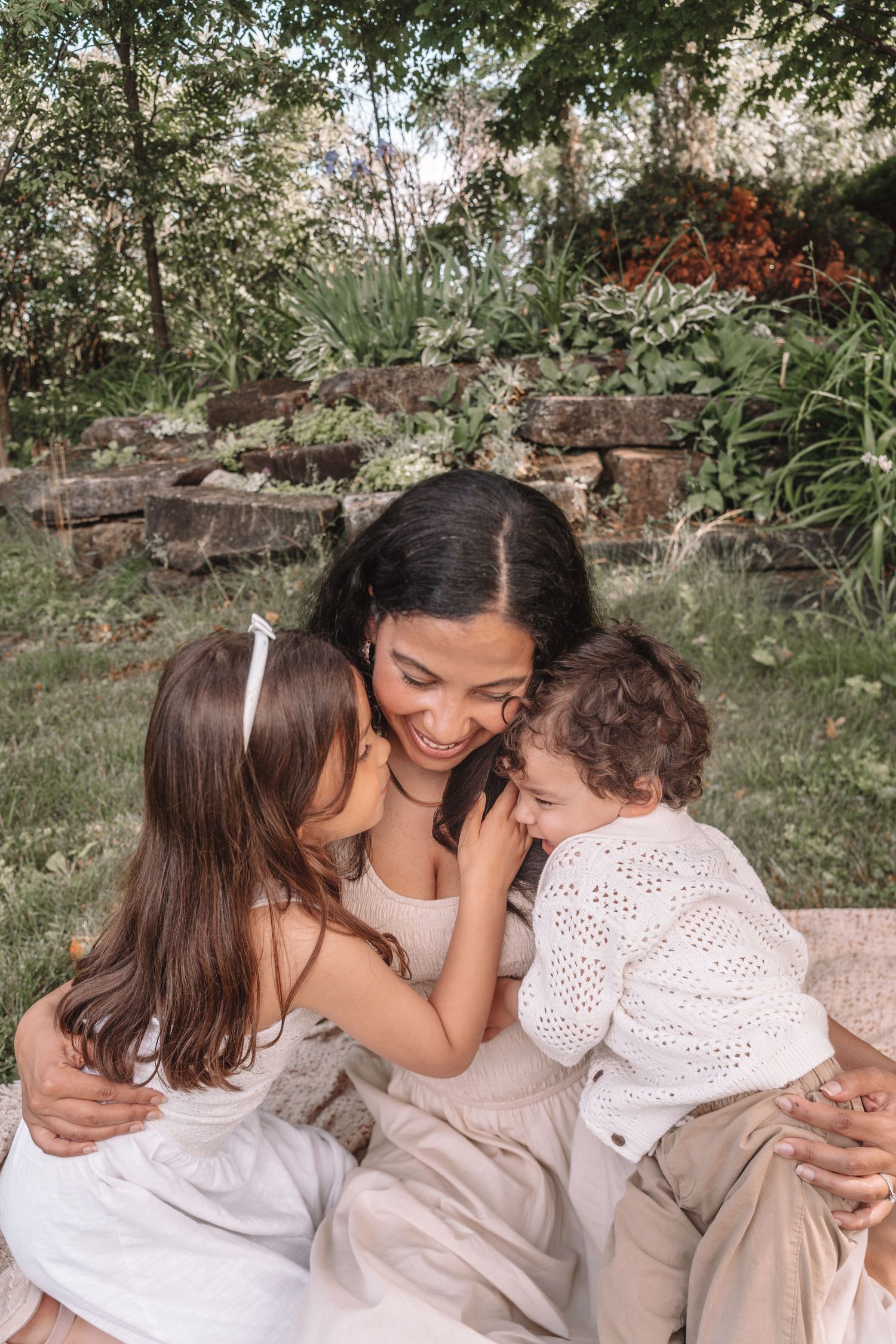 Mother embracing her two young daughters outdoors during a natural, candid spring family photography session in Kingston, Ontario.