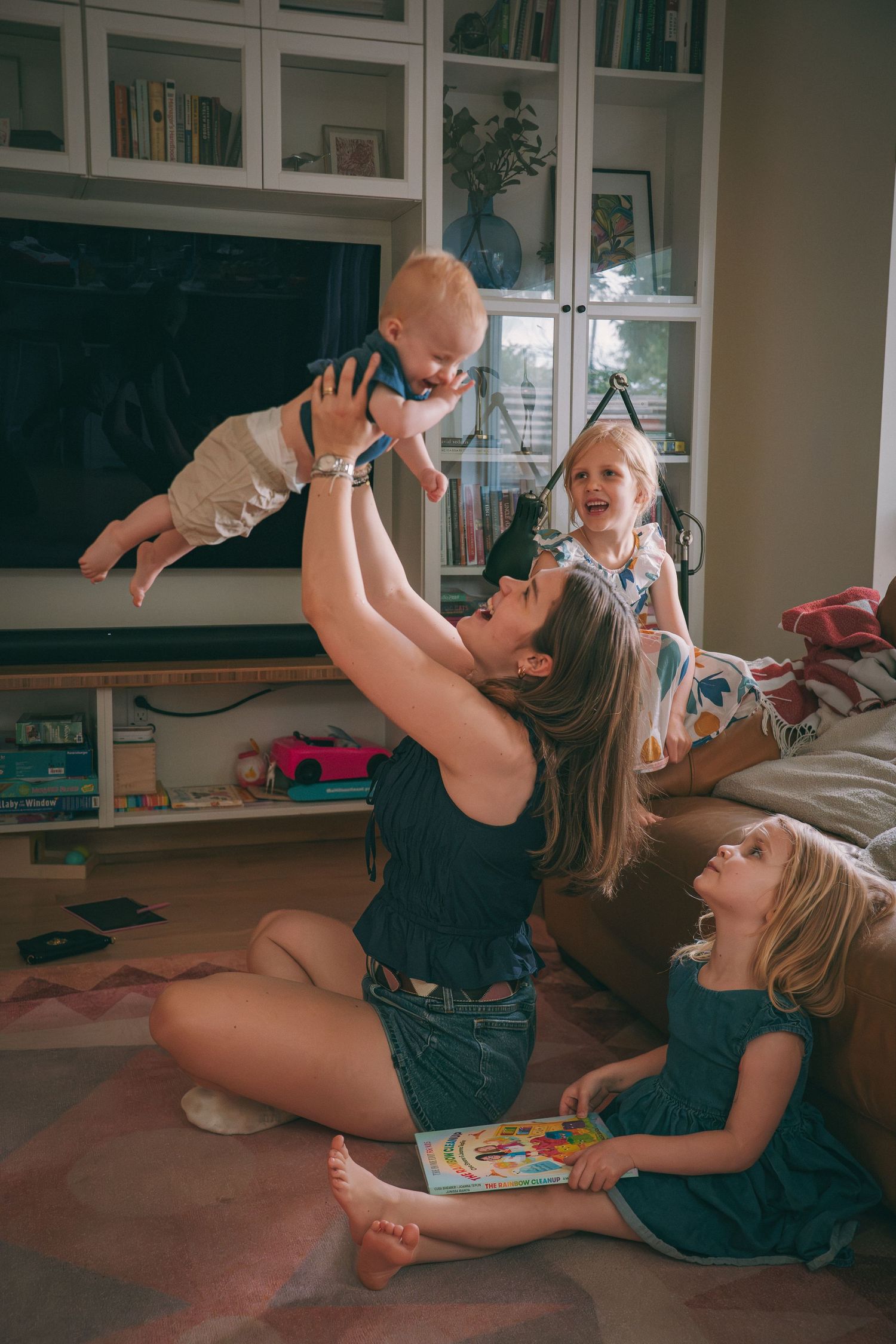 Parents playing with their baby while their child watches during a candid at-home lifestyle family photoshoot in Kingston, Ontario.