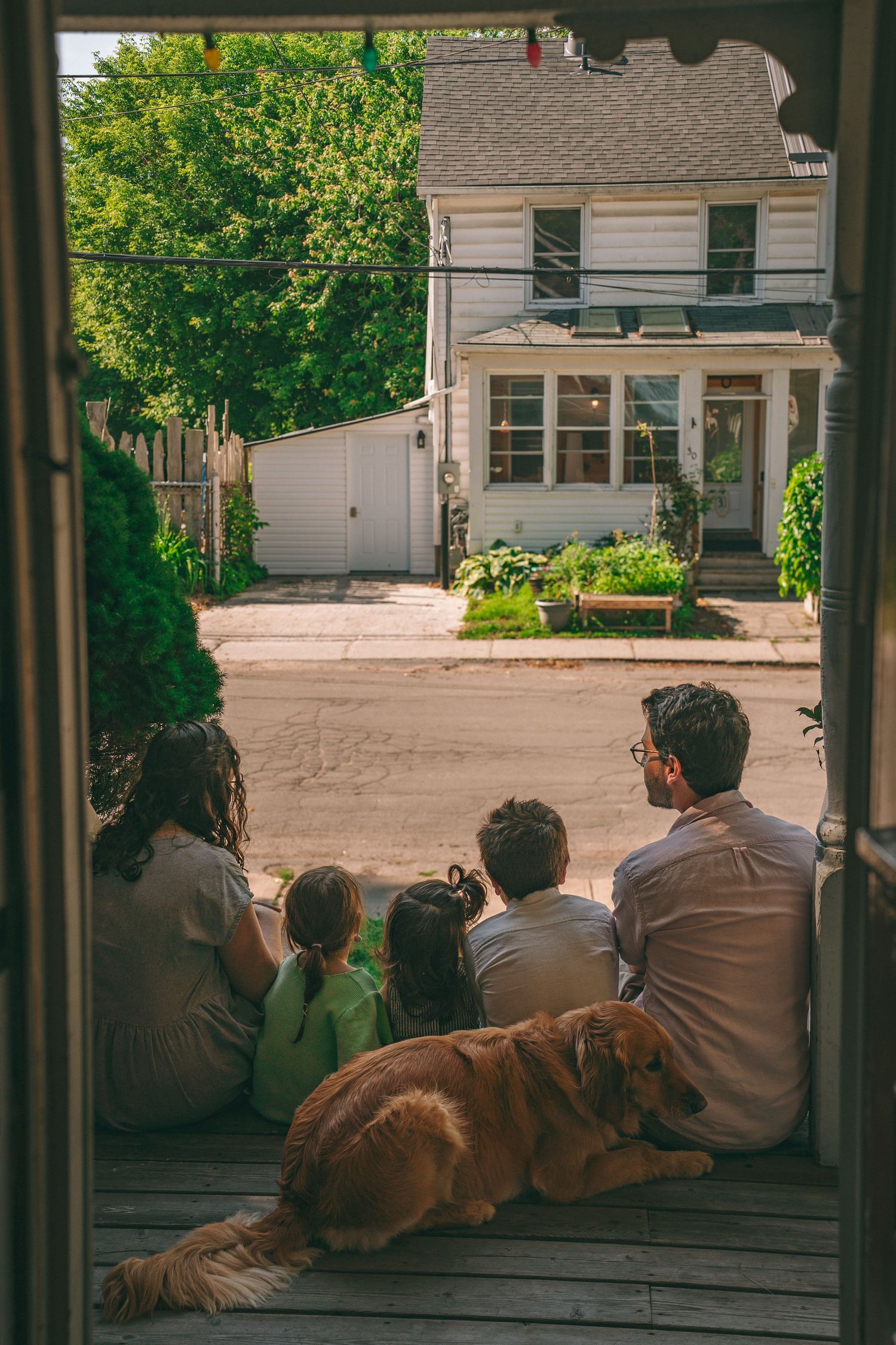 Family relaxing together with their dog on a wooden front porch during a natural lifestyle family photo summer session in Kingston, Ontario.