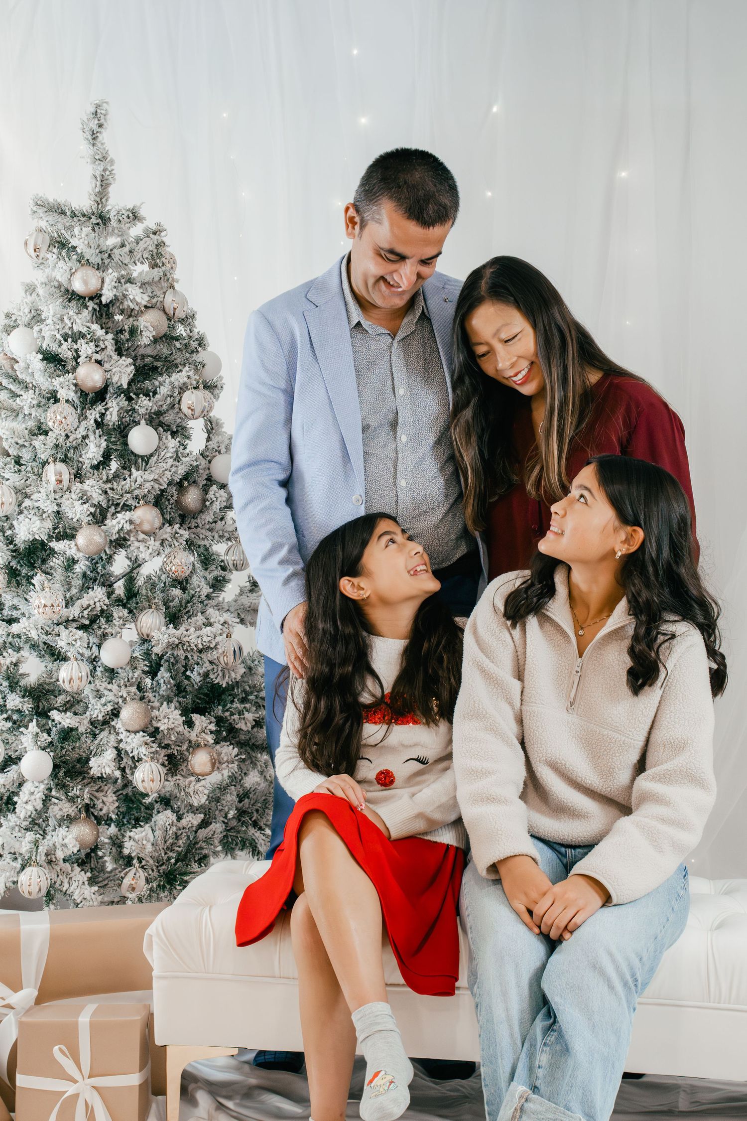 Family of four posing together in front of snow-covered Christmas trees during an indoor Christmas family photoshoot in Kingston, Ontario.