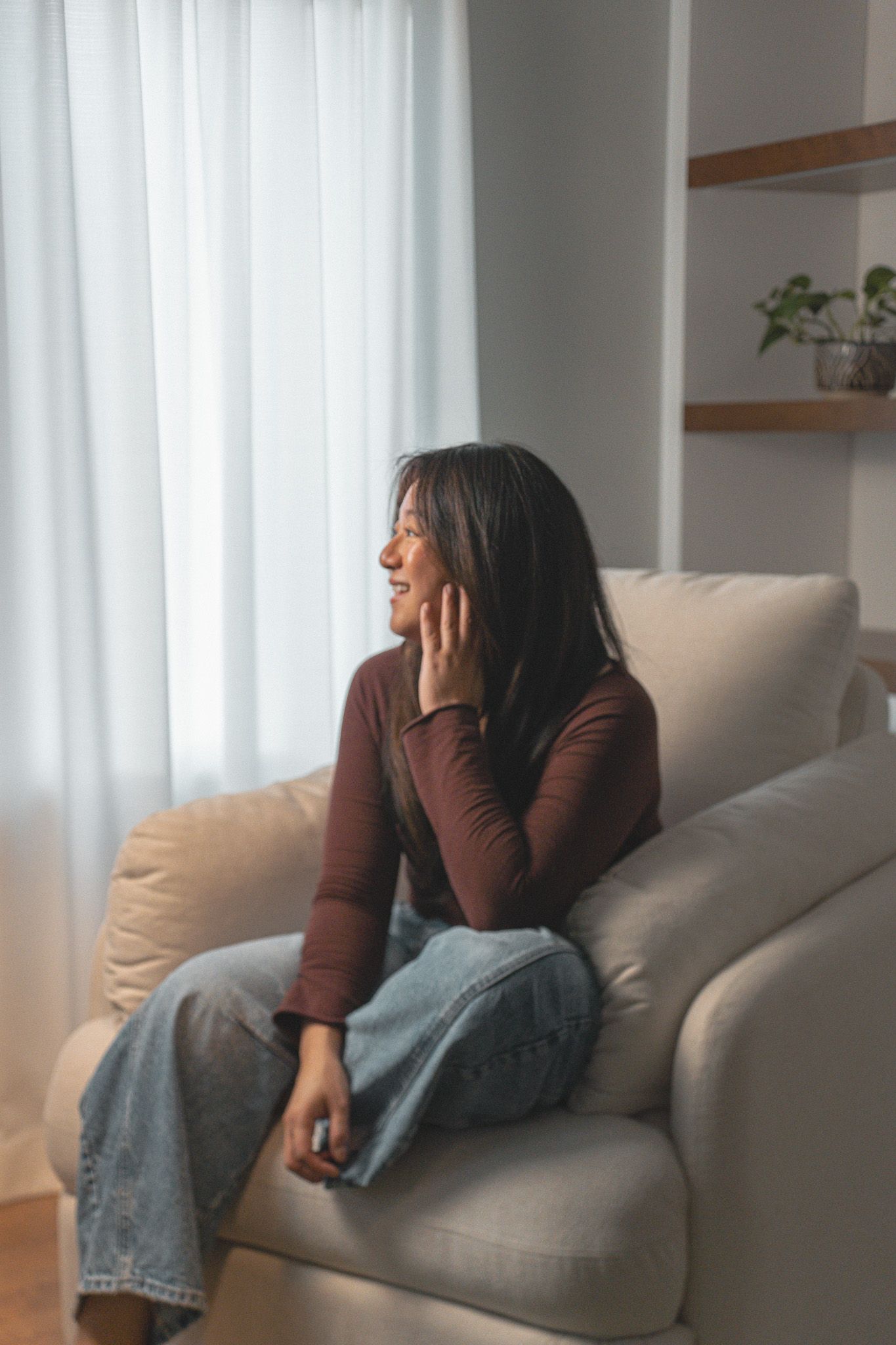 Indoor lifestyle portrait of a woman sitting by a window on a cozy armchair, photographed by Twy Photography in Kingston, Ontario.