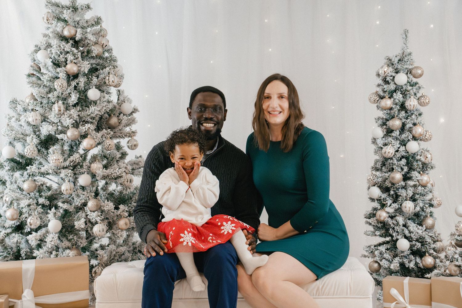 Family of three enjoying an indoor Christmas mini photo session with snowy Christmas trees at Twy Photography in Kingston, Ontario.