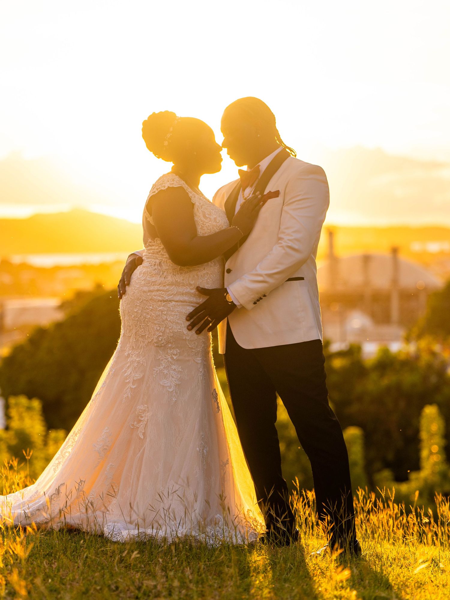 A couple embraces in a golden field during sunset, with soft light illuminating their romantic silhouettes.