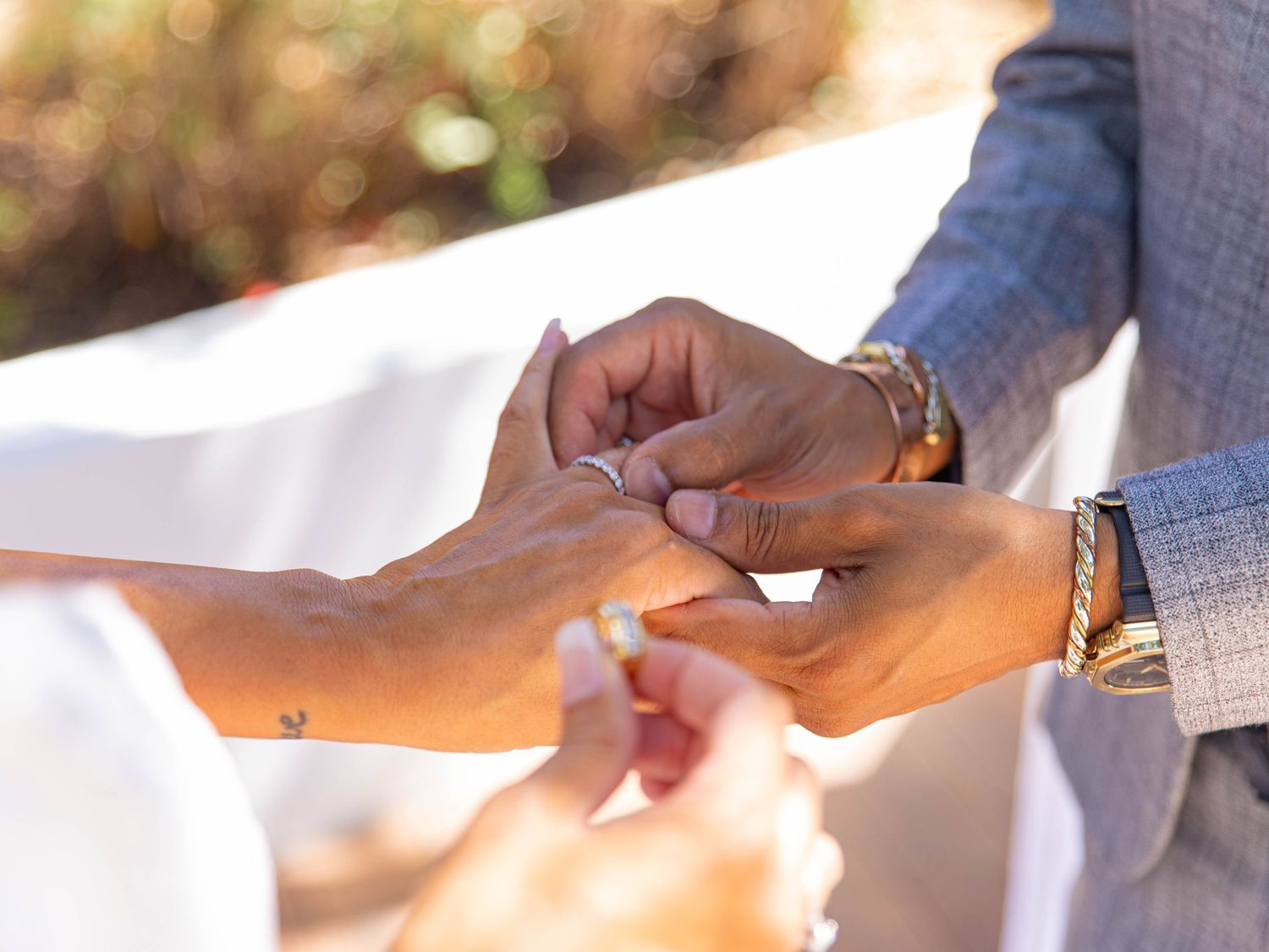Close-up of hands exchanging wedding rings during outdoor ceremony with soft natural lighting in background.