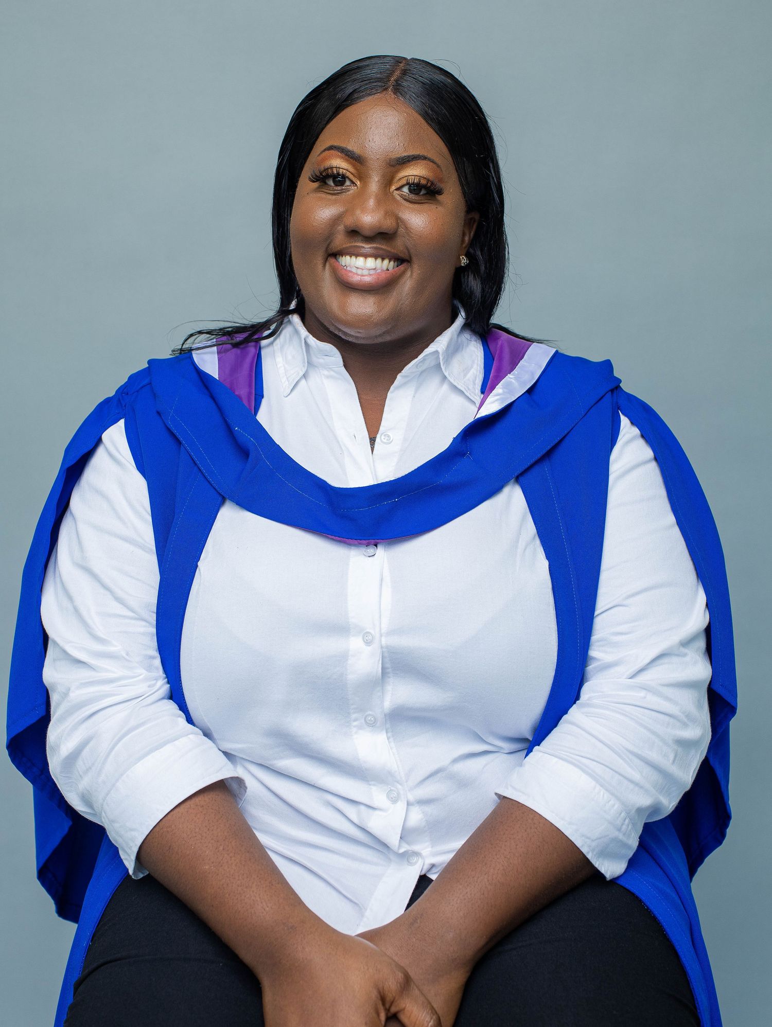 Graduate wearing academic regalia with blue hood poses for portrait against gray background.