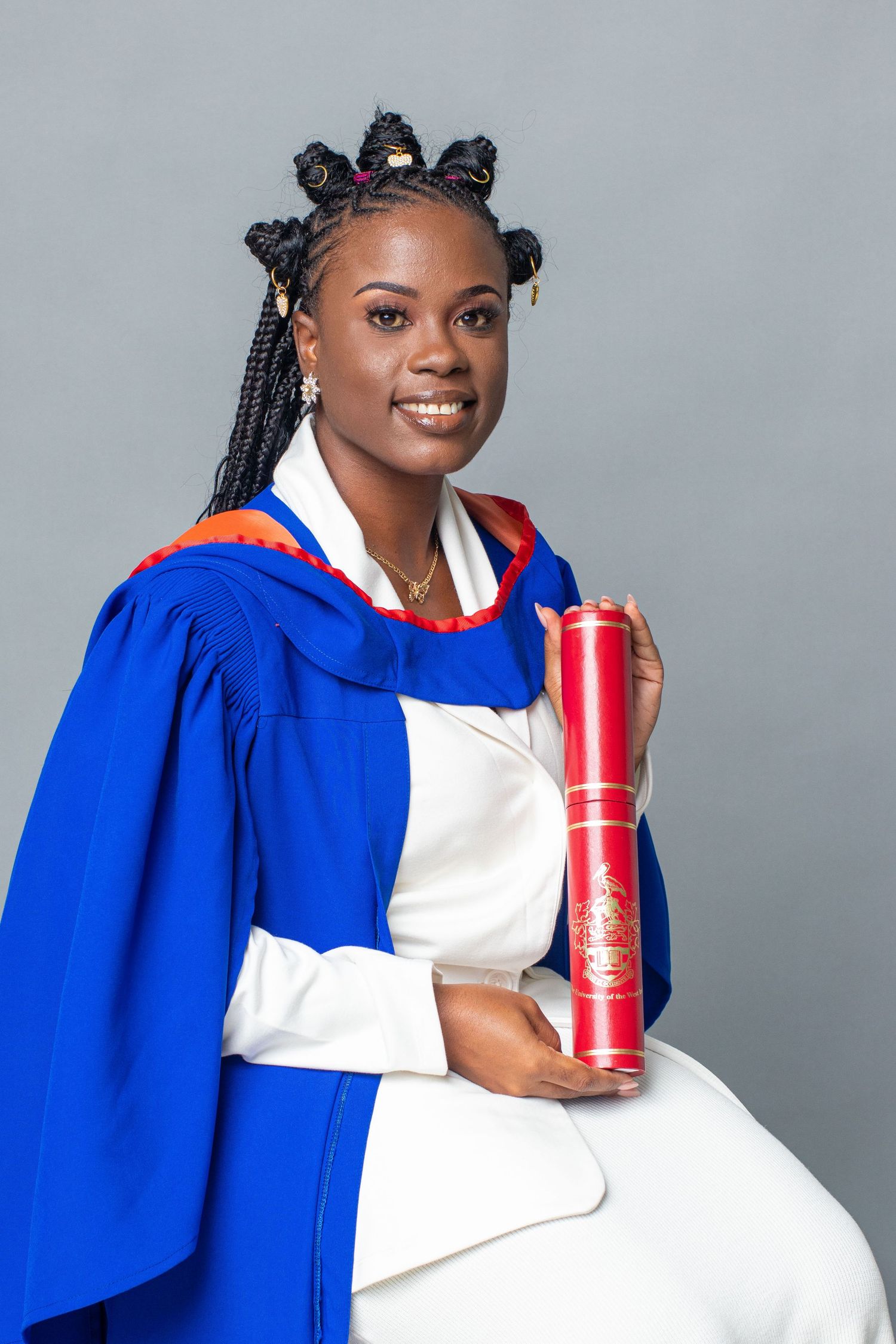 Graduate in blue academic regalia holds red diploma case while posing for portrait.