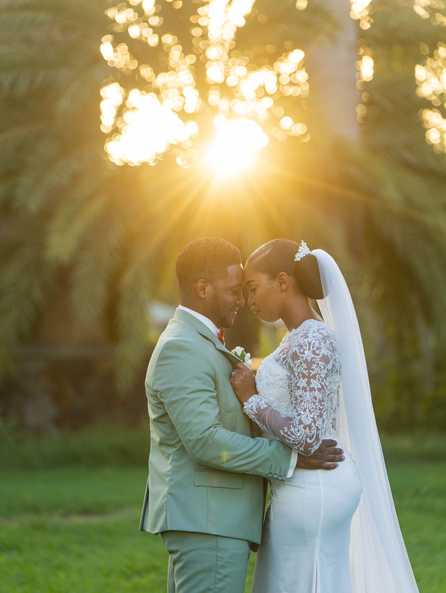 A romantic wedding couple embraces during golden hour sunset with palm trees creating a magical backlit glow.