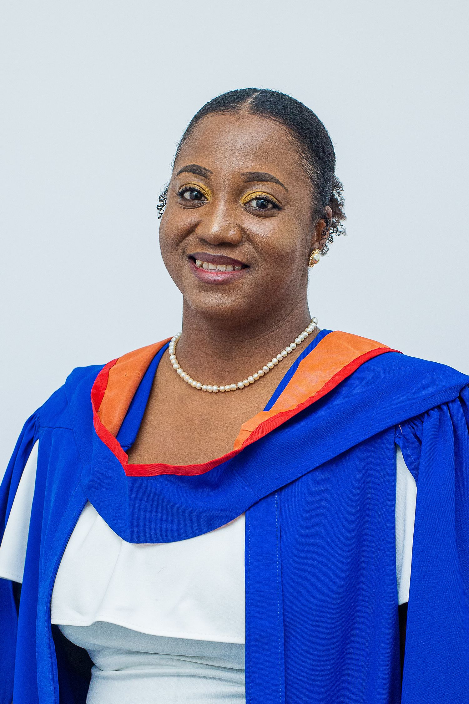 Graduate in blue and orange academic regalia wearing pearl necklace with warm smile.