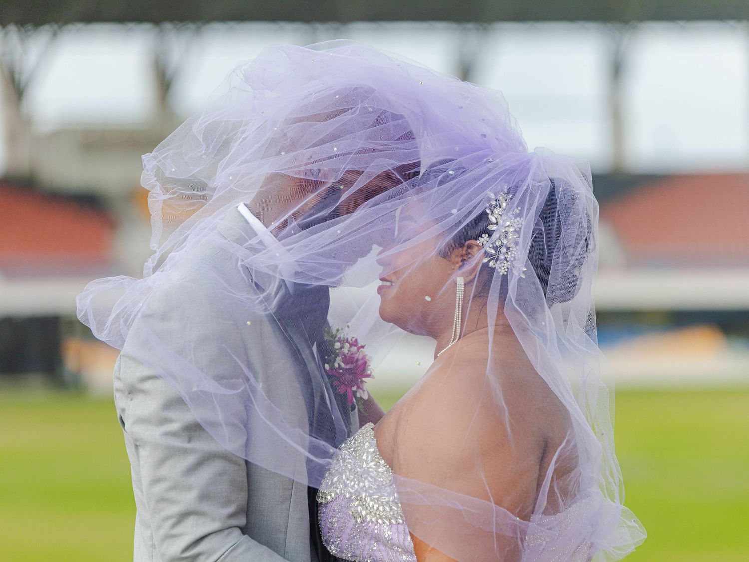 A delicate lavender veil flows in the wind against a blurred outdoor background.