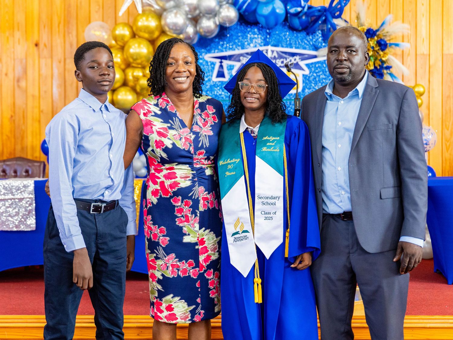 Family of four posing together at a graduation ceremony with blue and gold balloon decorations in the background.