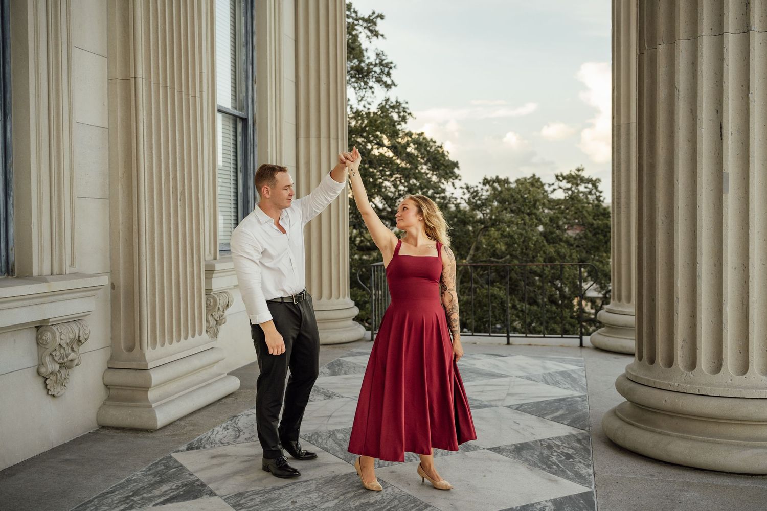Couple dancing and twirling on a stone terrace with columns, the woman in a flowing burgundy dress.