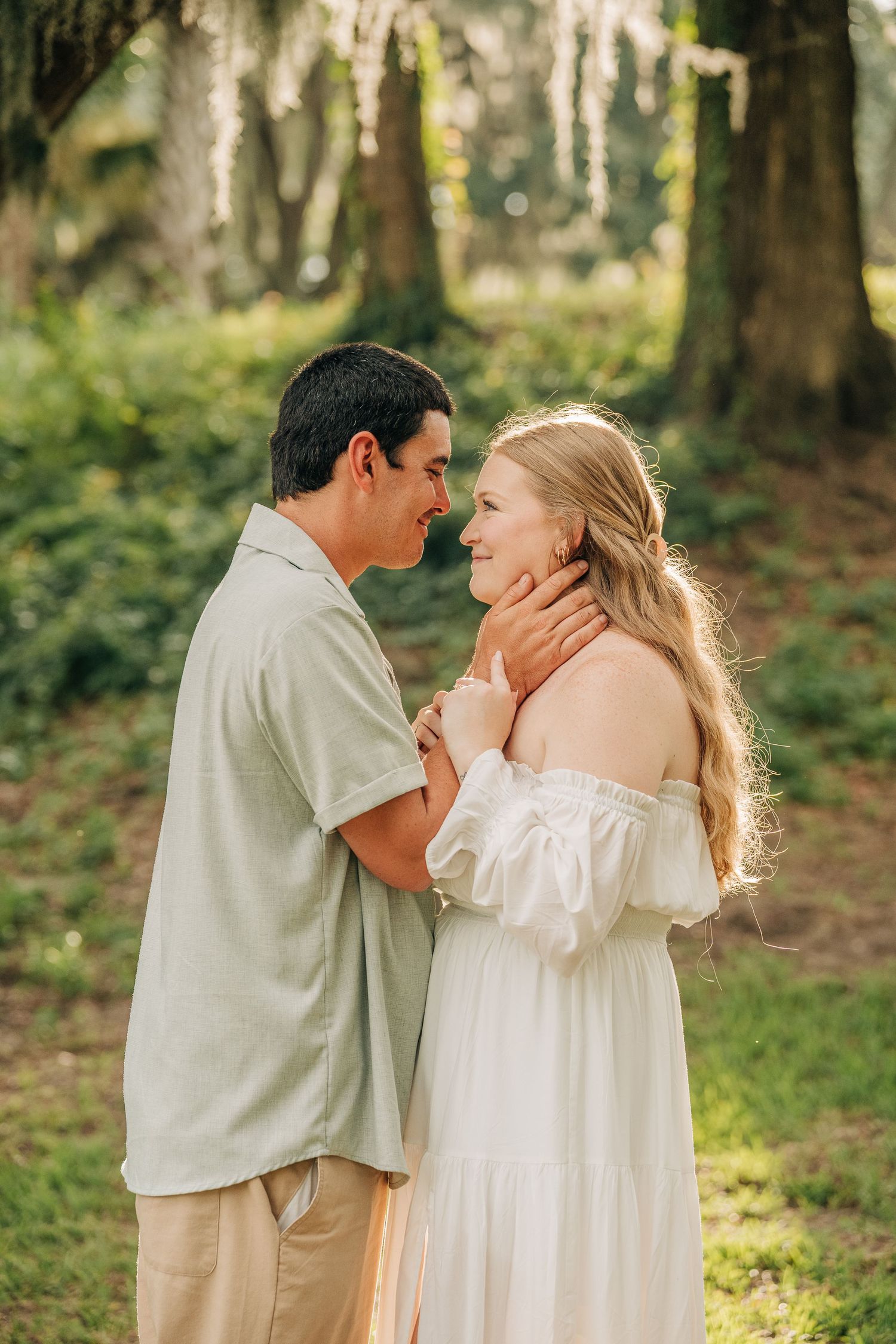 Smiling couple gazing at each other in a green woodland setting during an outdoor engagement photo session.