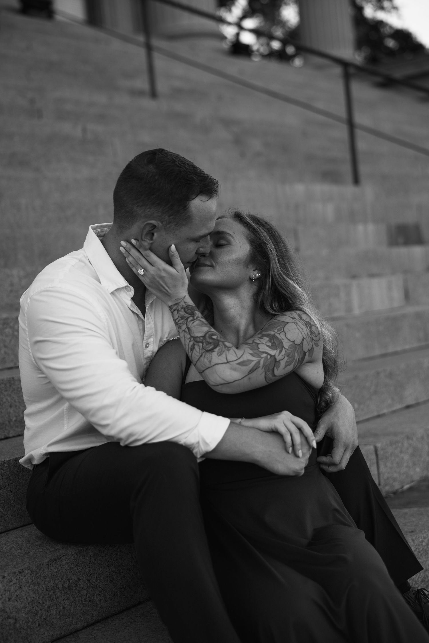 Black and white photo of a couple kissing tenderly on stone steps, the man's hand gently cupping the woman's face.