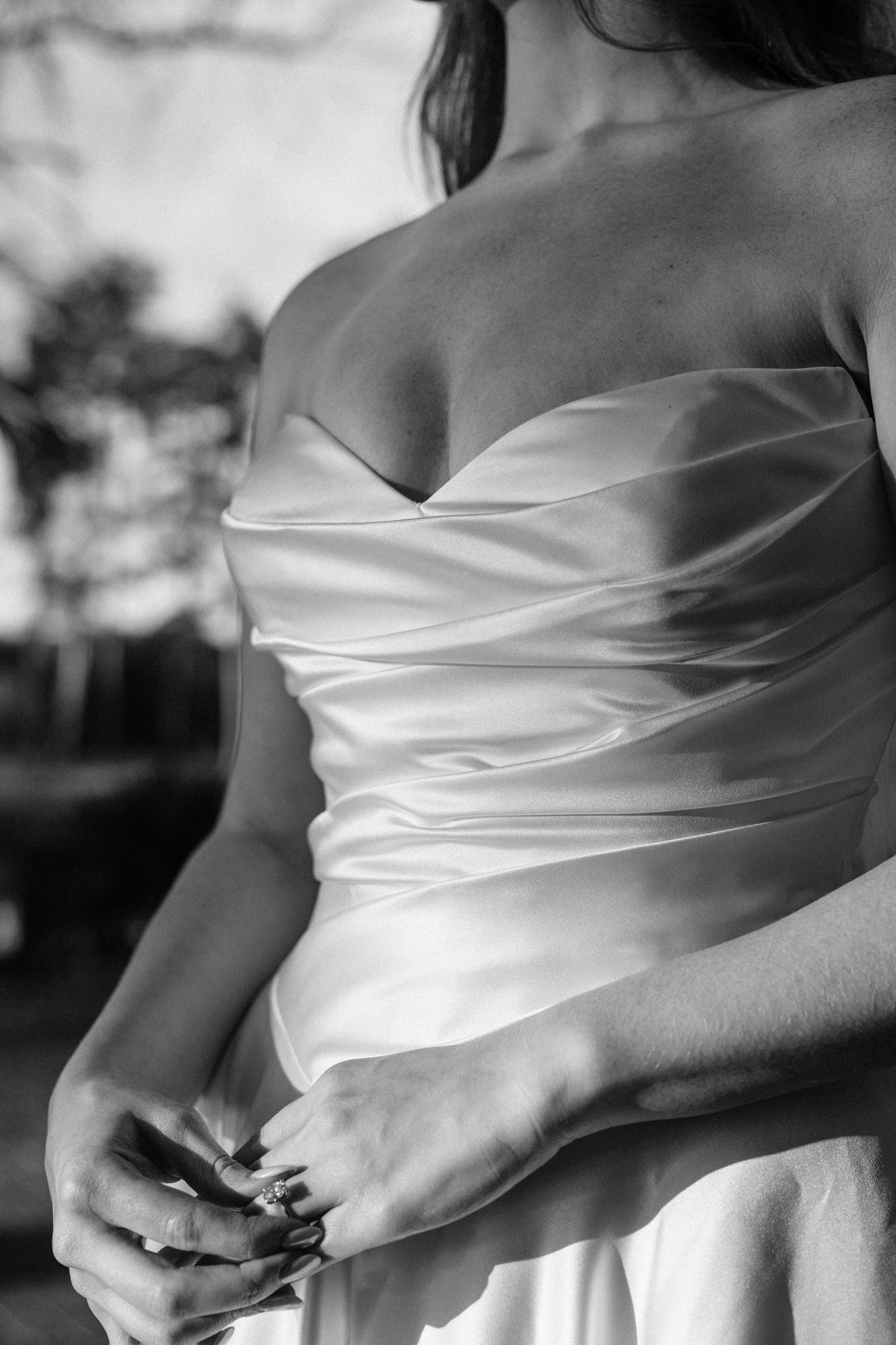 Black and white close-up of a bride's sweetheart neckline satin bodice as she clasps her hands showing her rings.