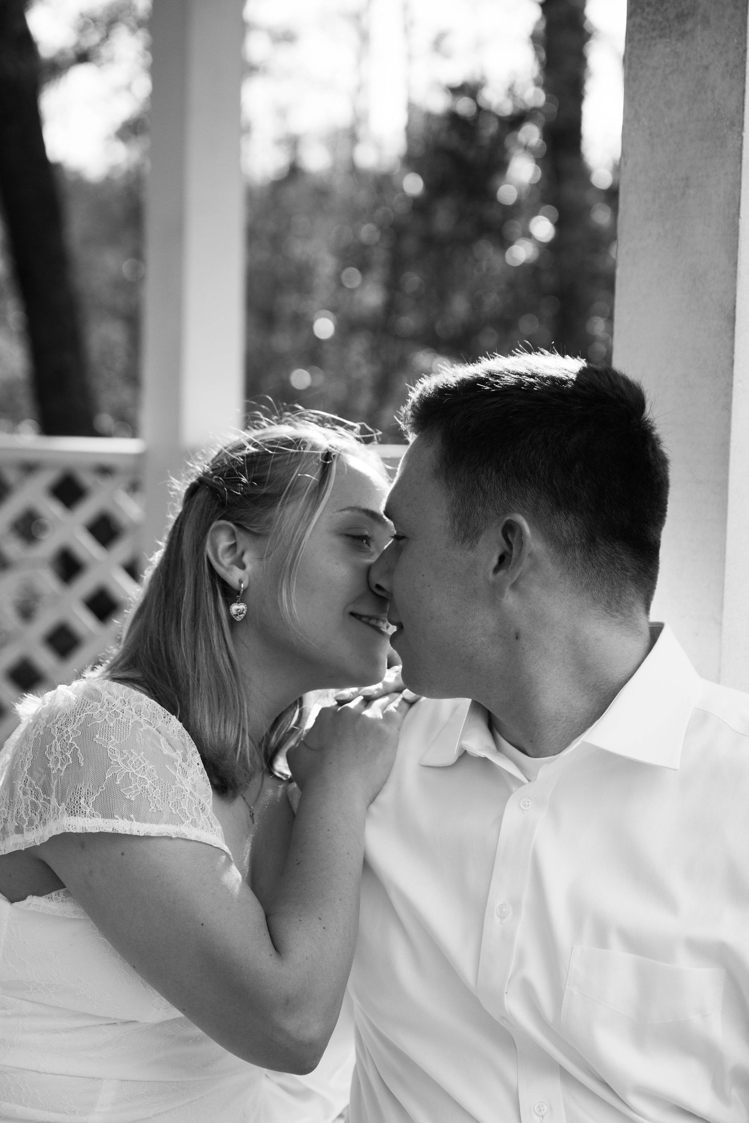 Black and white close-up of a couple about to kiss, the woman's hand on the man's shoulder in a garden gazebo.