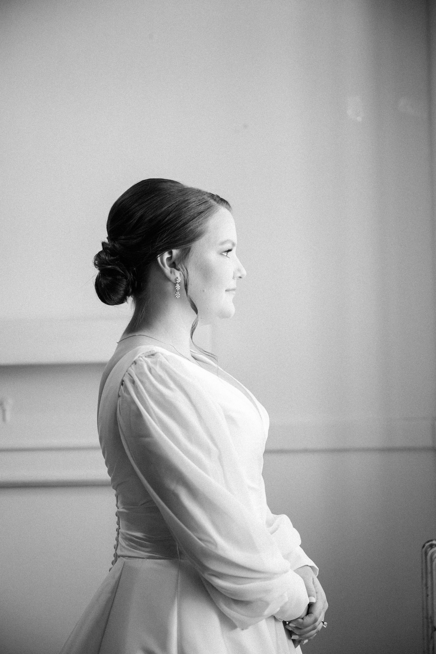 Black and white profile portrait of a bride in a sheer-sleeved gown with an elegant low bun and drop earrings gazing aside.
