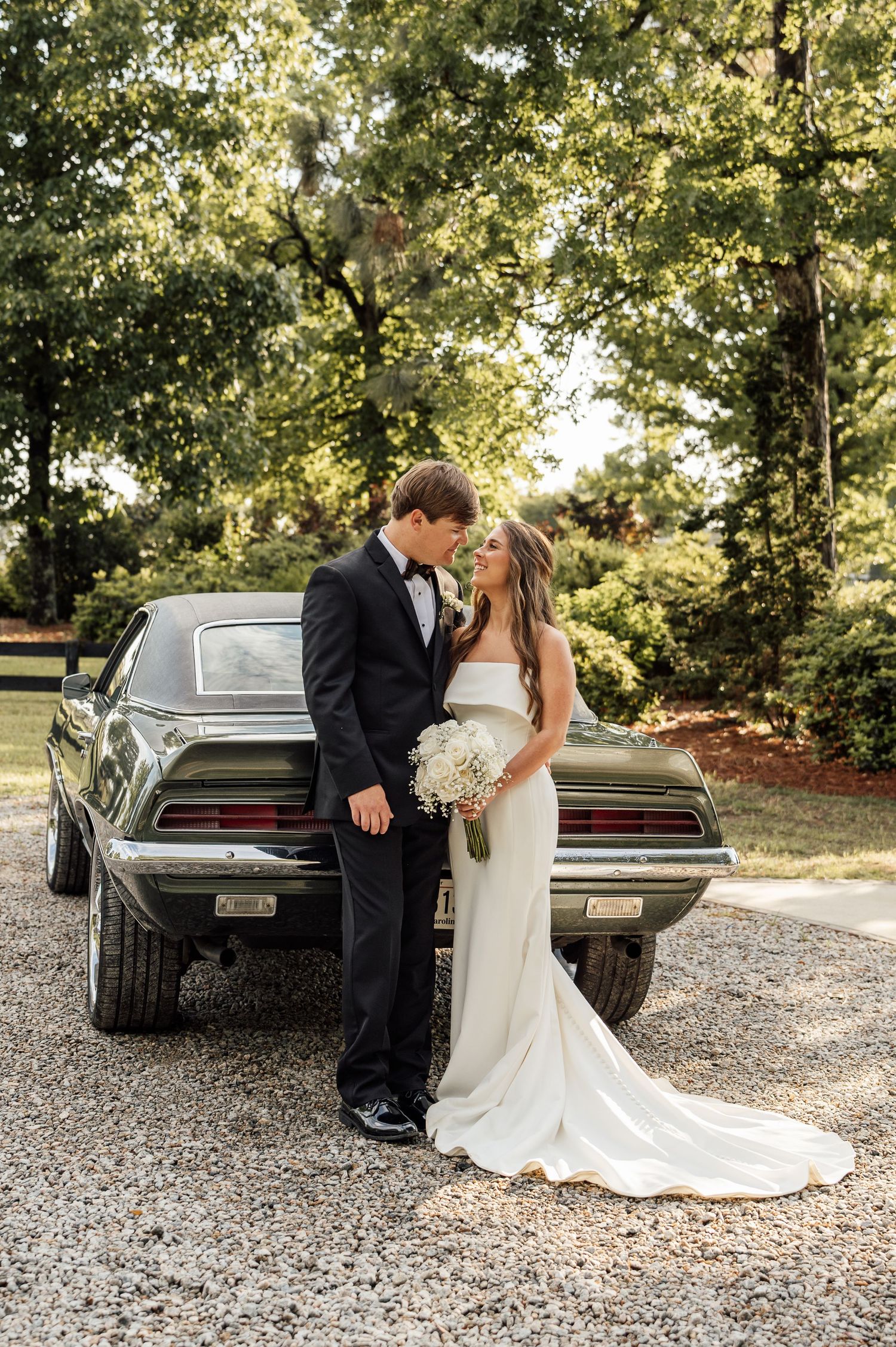 Bride and groom posing together outdoors beside a vintage vehicle on their wedding day.